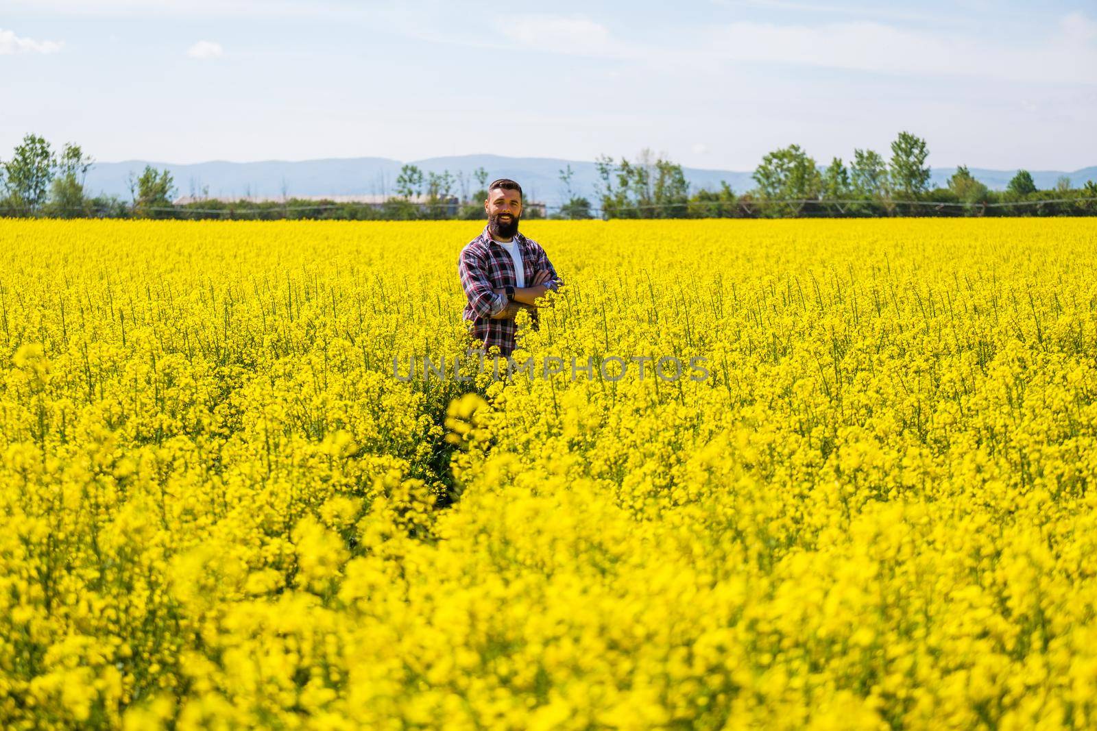 Portrait of happy and successful farmer who is standing in his rapeseed field. Rapeseed plantation in bloom.