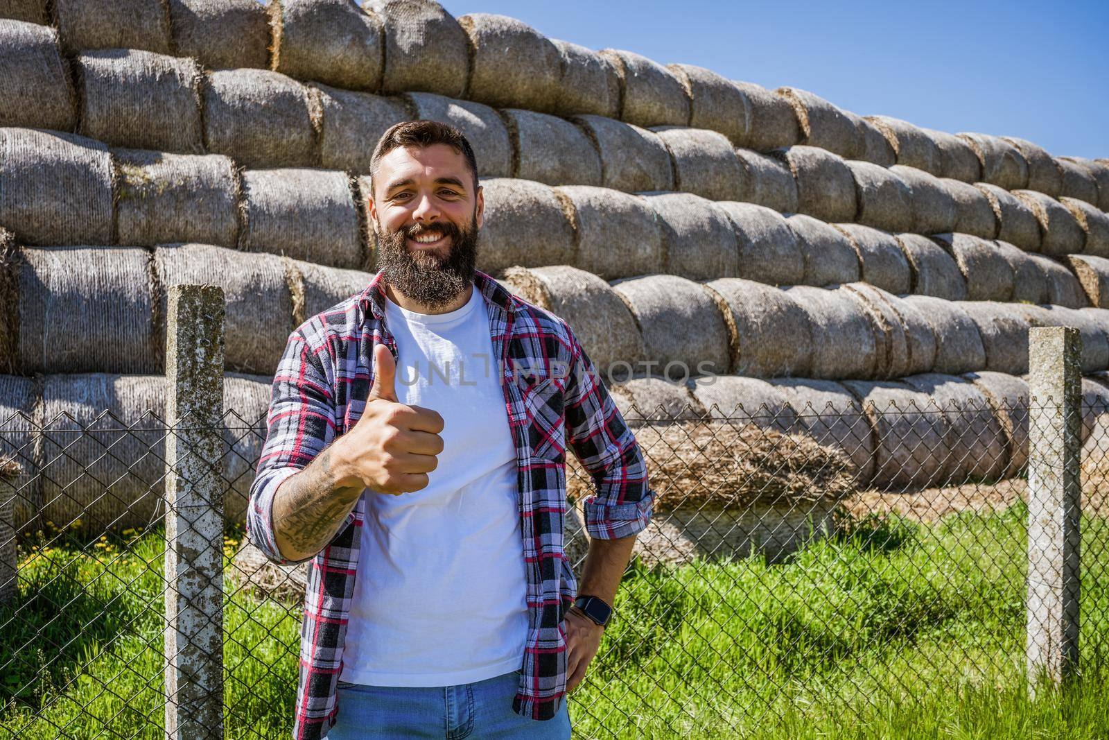 Happy farmer is standing beside bales of hay.