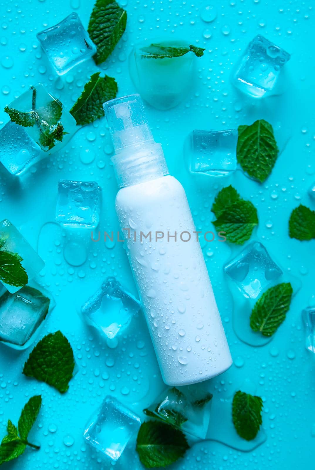 Bottle with cosmetics on a mint background with ice cubes. Selective focus. by yanadjana