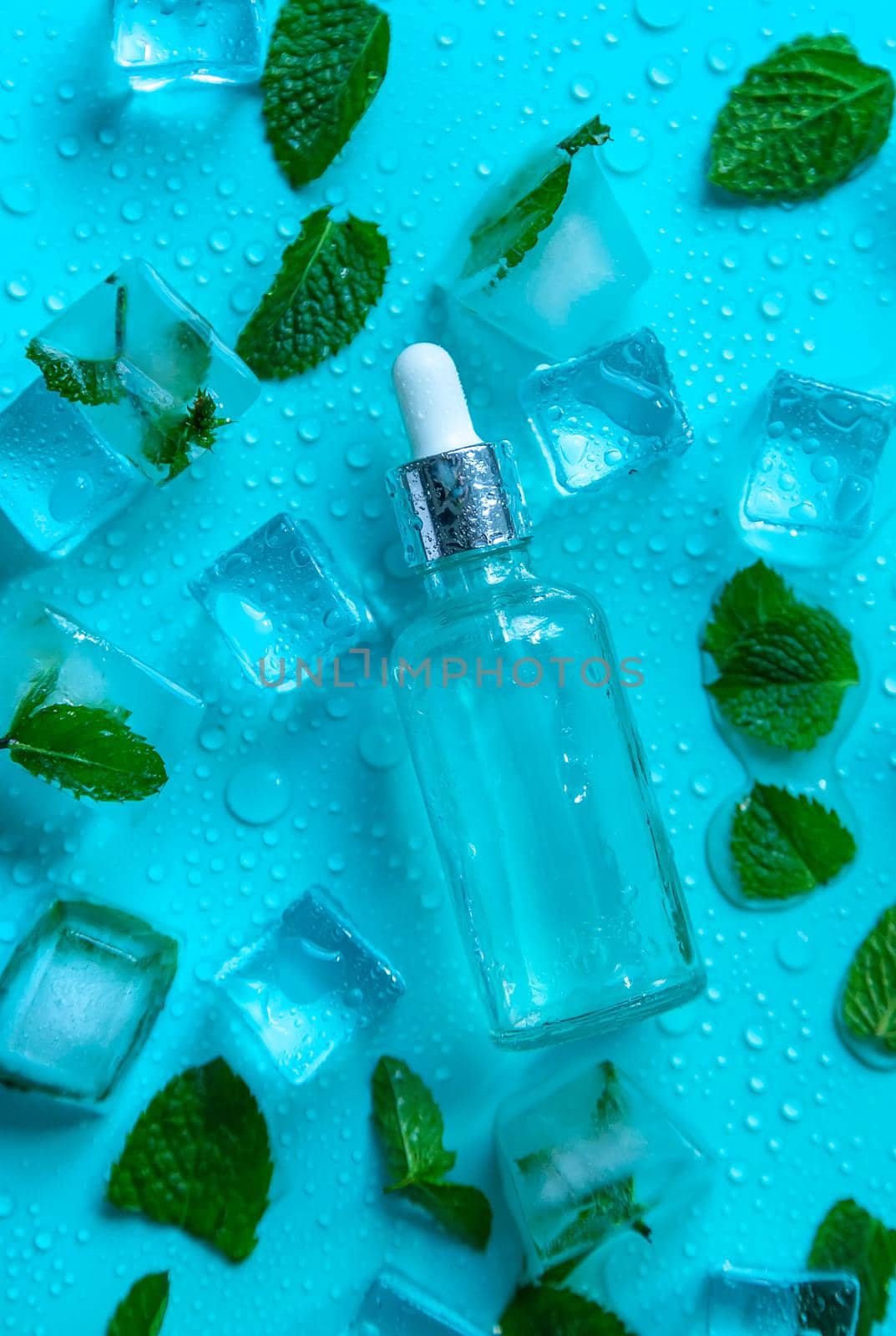 Bottle with cosmetics on a mint background with ice cubes and lemon. Selective focus. by yanadjana