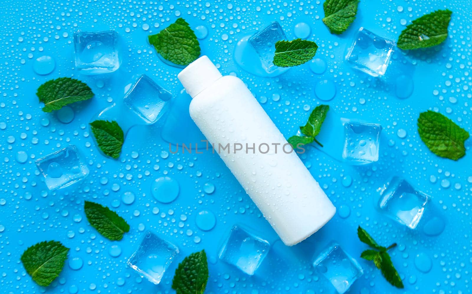 Bottle with cosmetics on a mint background with ice cubes. Selective focus. by yanadjana
