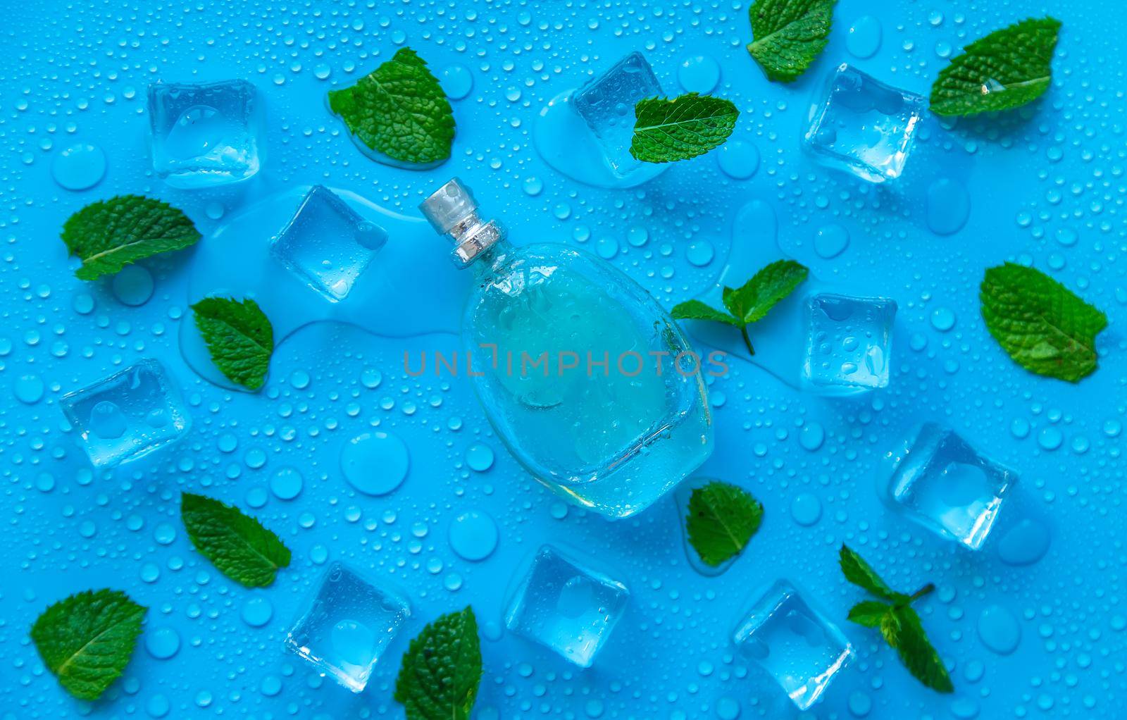 Perfume on a blue background with ice cubes and mint. Selective focus. by yanadjana