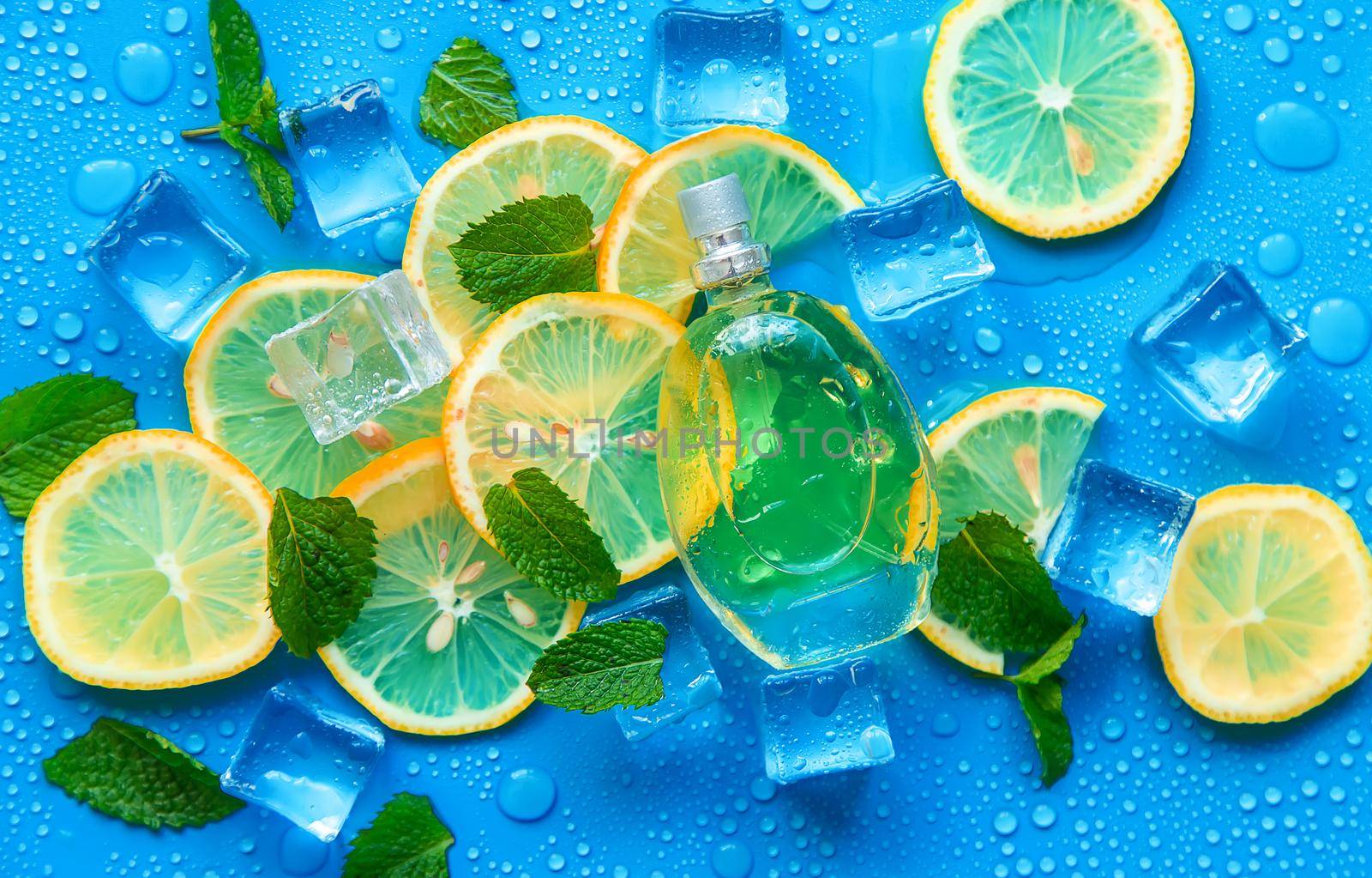 Perfume on a blue background with ice cubes and mint lemon. Selective focus. by yanadjana