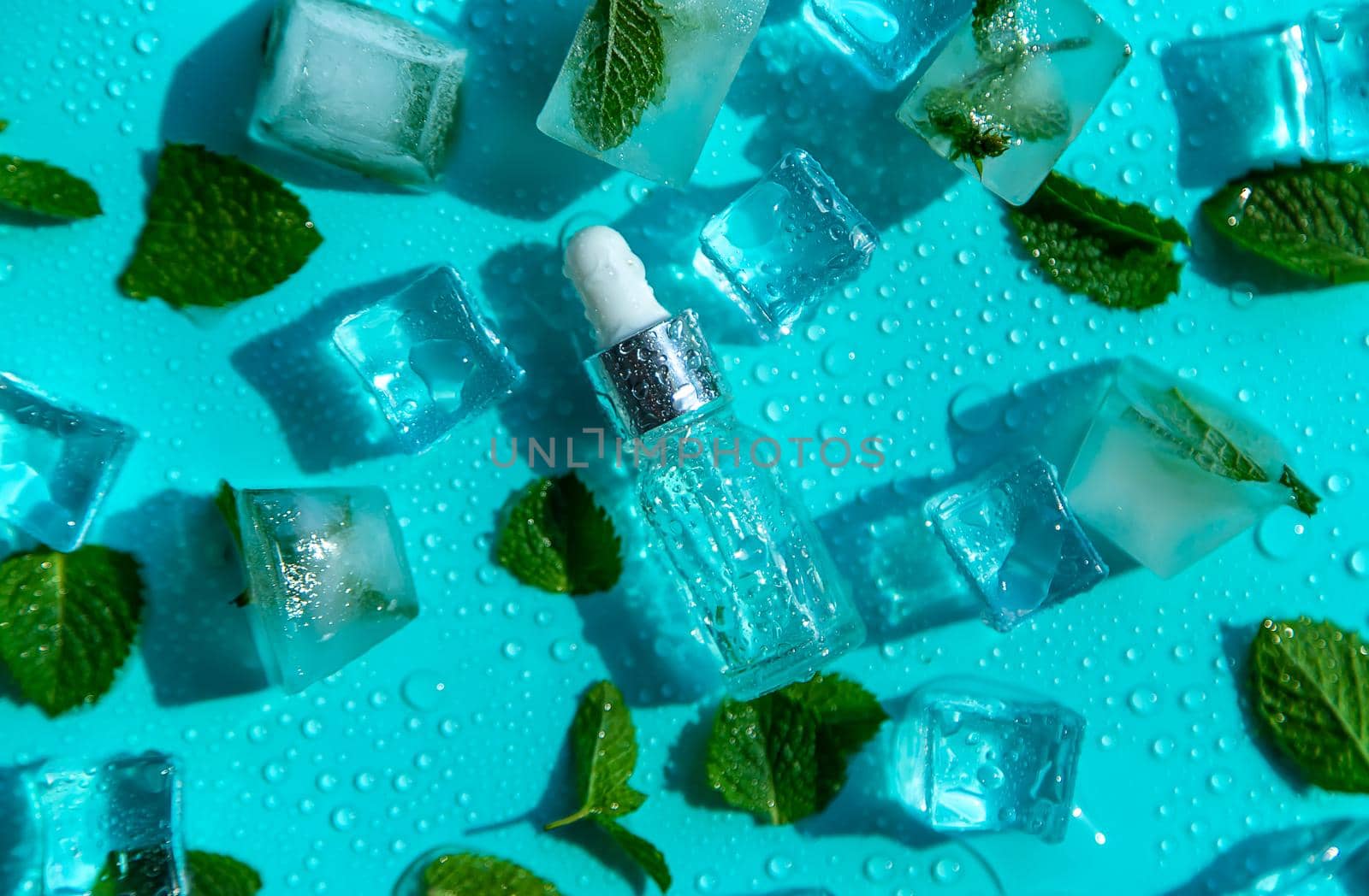 Bottle with cosmetics on a mint background with ice cubes and lemon. Selective focus. Spa.