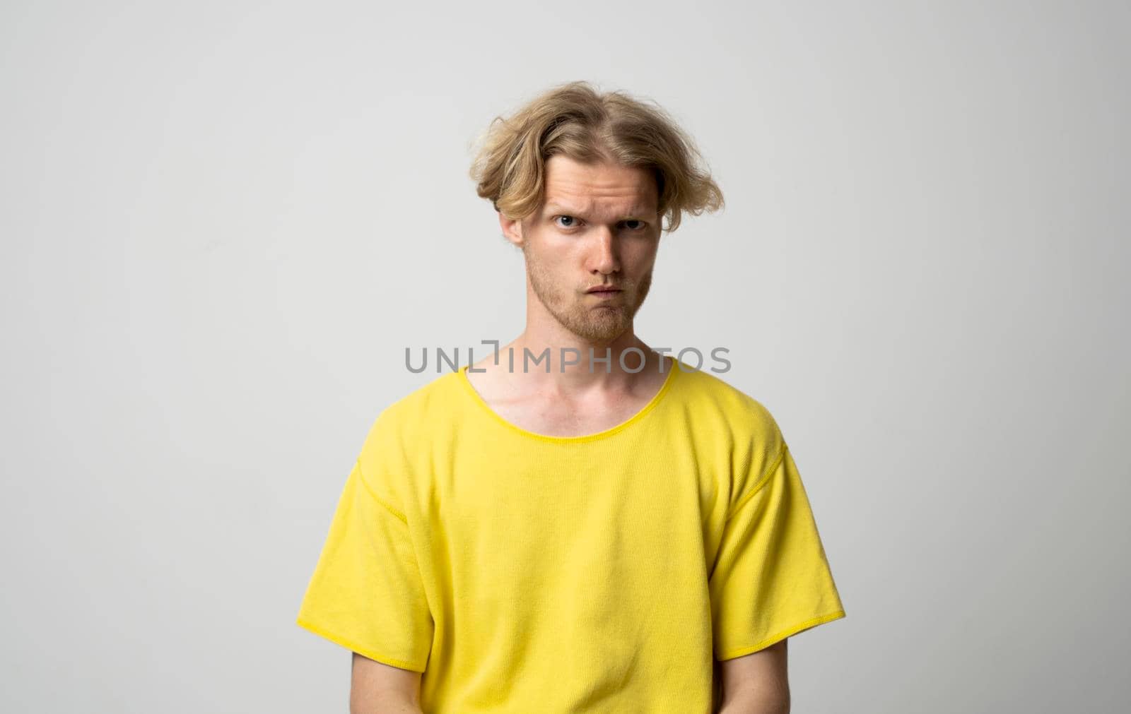 Closeup portrait of angry young man. Portrait of upset young man a yellow t-shirt standing with arms folded isolated over white background. Emotion of angry and upset
