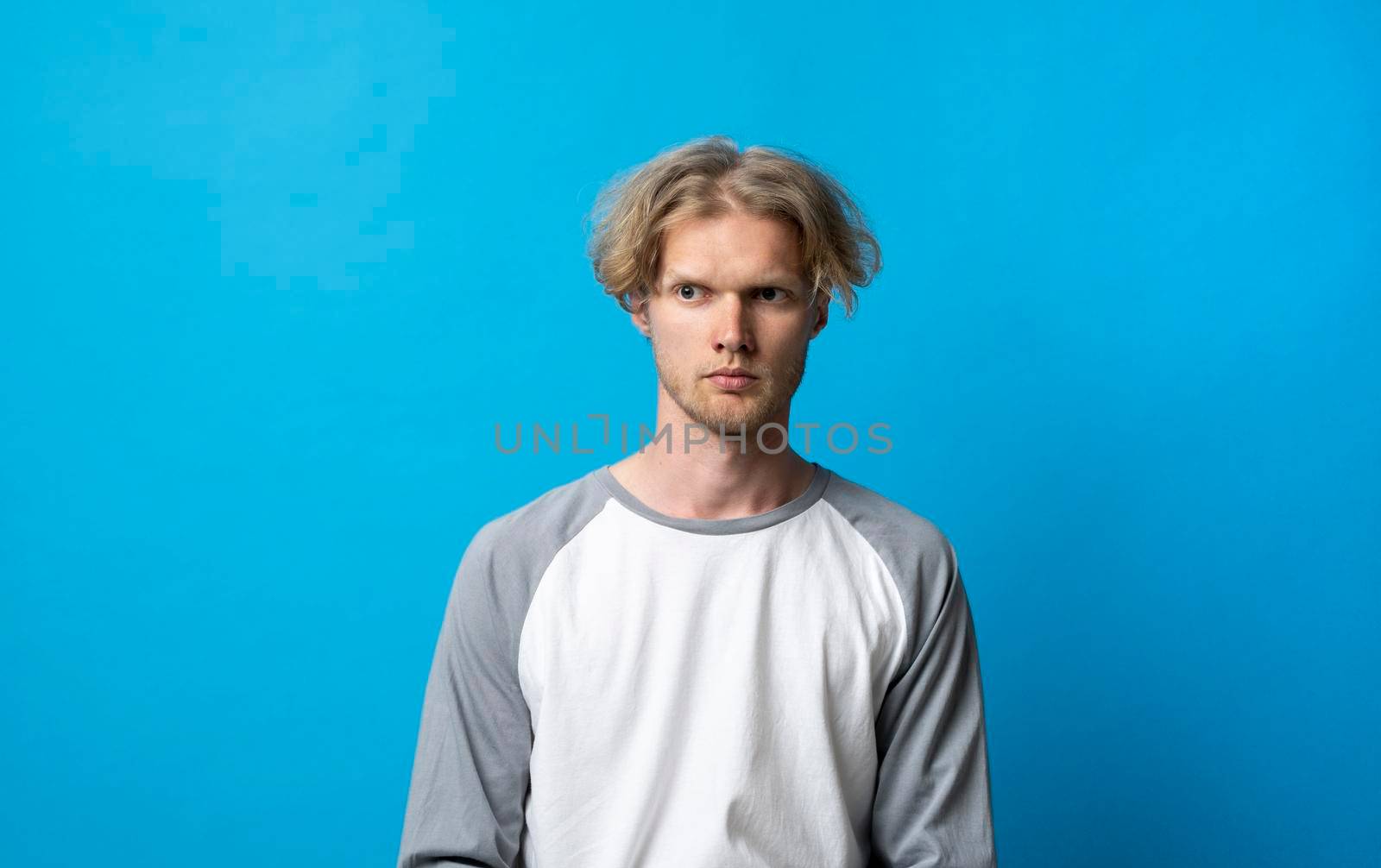 Man with long hair frowning her face in displeasure, wearing yellow t-shirt. Attractive young man in angry posture. Negative human emotions facial expression feelings attitude