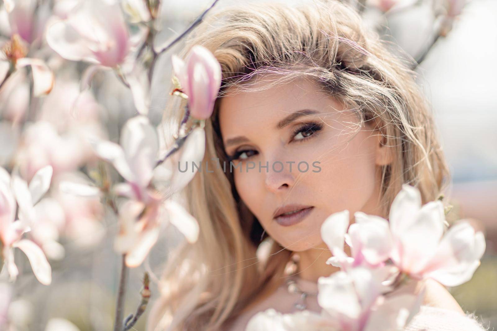 Portrait of a beautiful happy middle aged woman enjoying the smell in a blooming spring garden. Beautiful magnolia bushes, large flowers