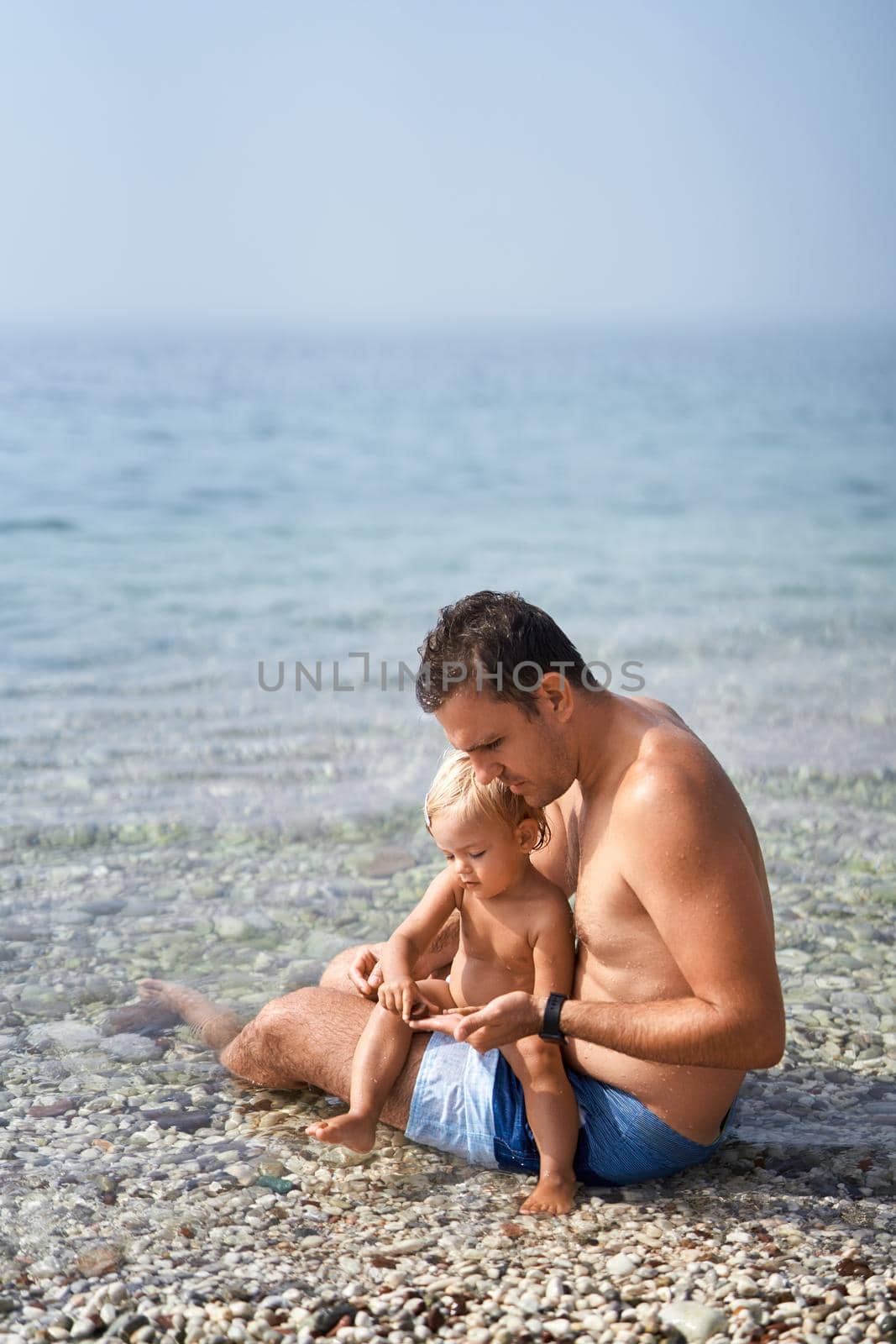 Dad and a little girl are sitting in shallow and sorting out sea pebbles. High quality photo