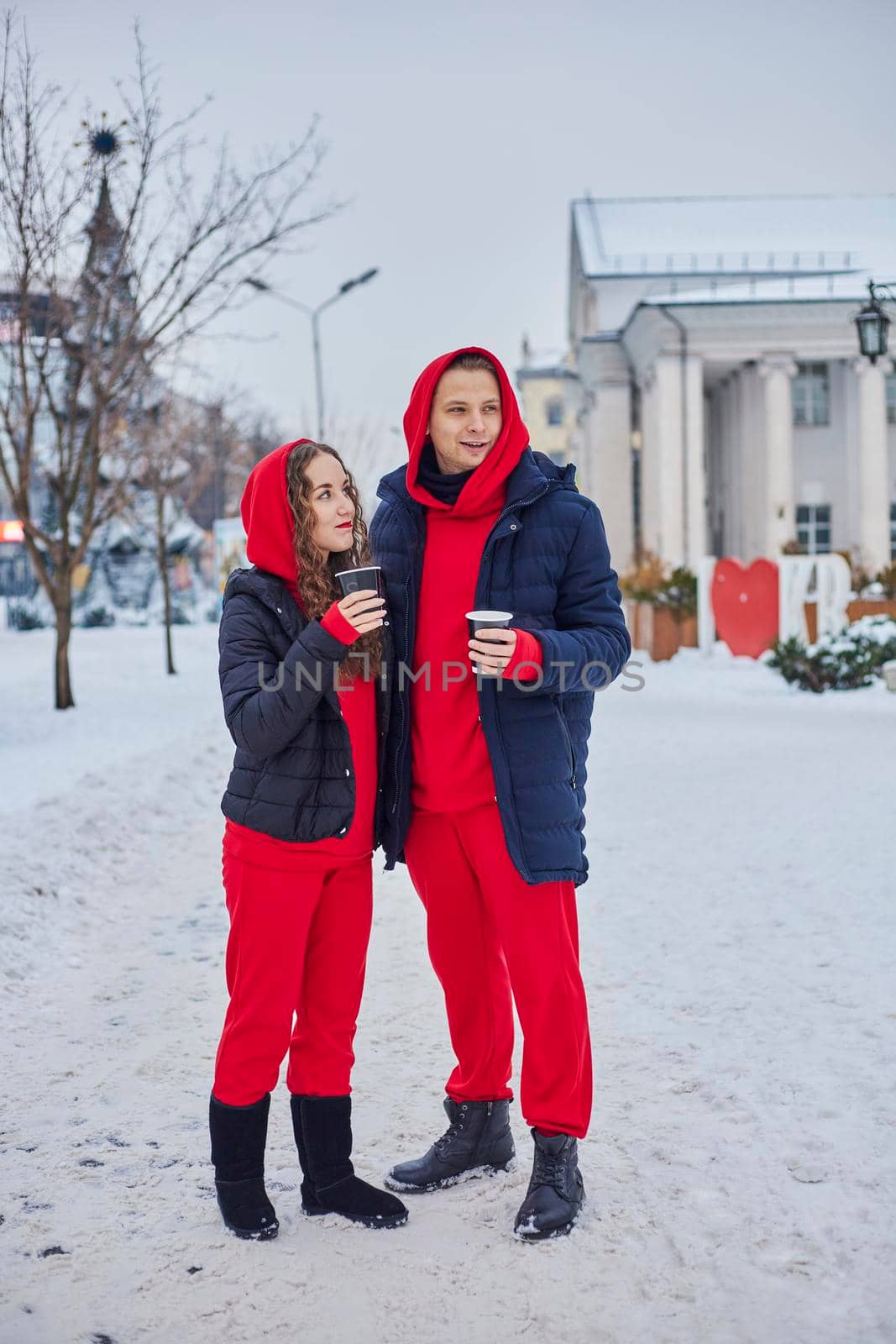 young family guy and girl spend the day in the park on a snowy day. the guy hugs the girl while standing on the street, they drink coffee together. by mosfet_ua