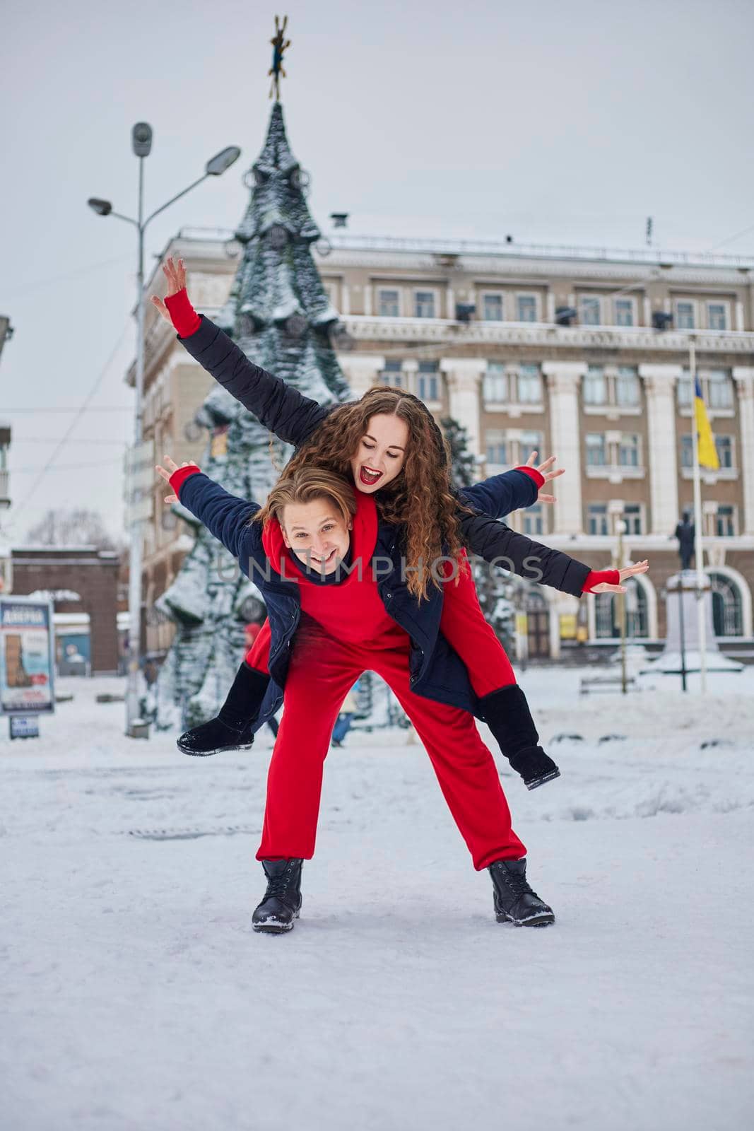 young family guy and girl spend the day in the park on a snowy day. Emotional young couple having fun while walking in the winter city, a lively man hugs his laughing beautiful woman. by mosfet_ua