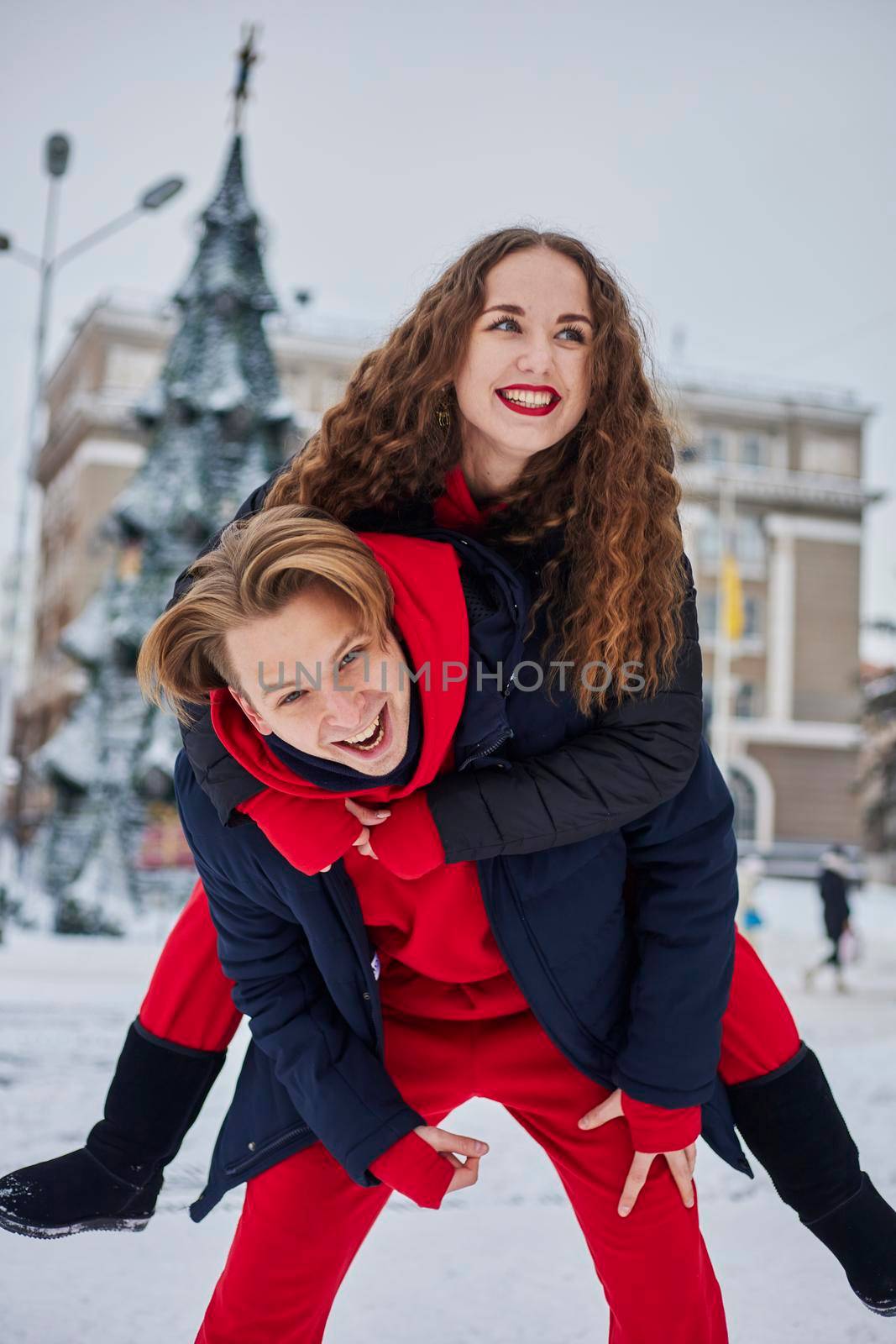 young family guy and girl spend the day in the park on a snowy day. Emotional young couple having fun while walking in the winter city, a lively man hugs his laughing beautiful woman