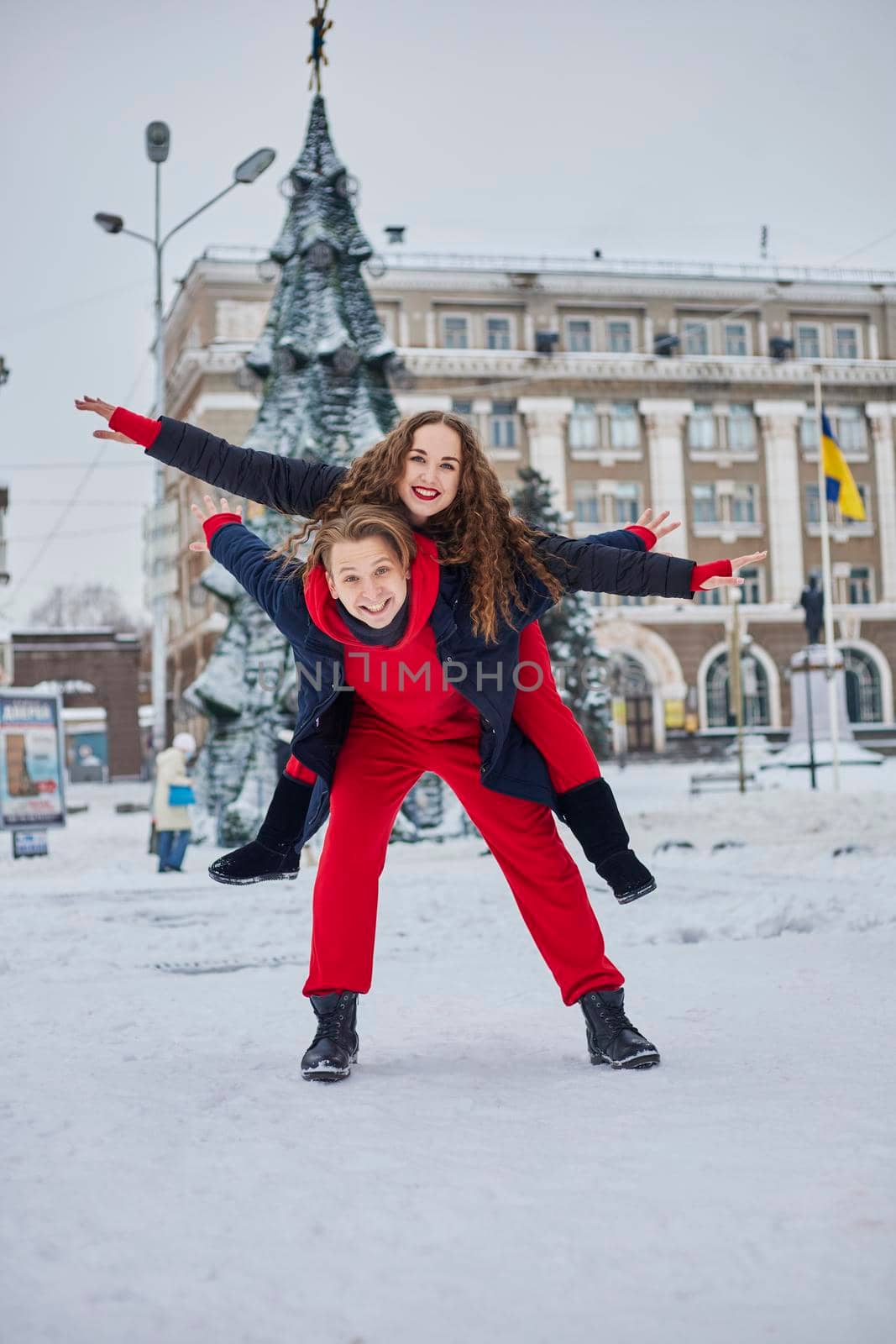 young family guy and girl spend the day in the park on a snowy day. Emotional young couple having fun while walking in the winter city, a lively man hugs his laughing beautiful woman. by mosfet_ua