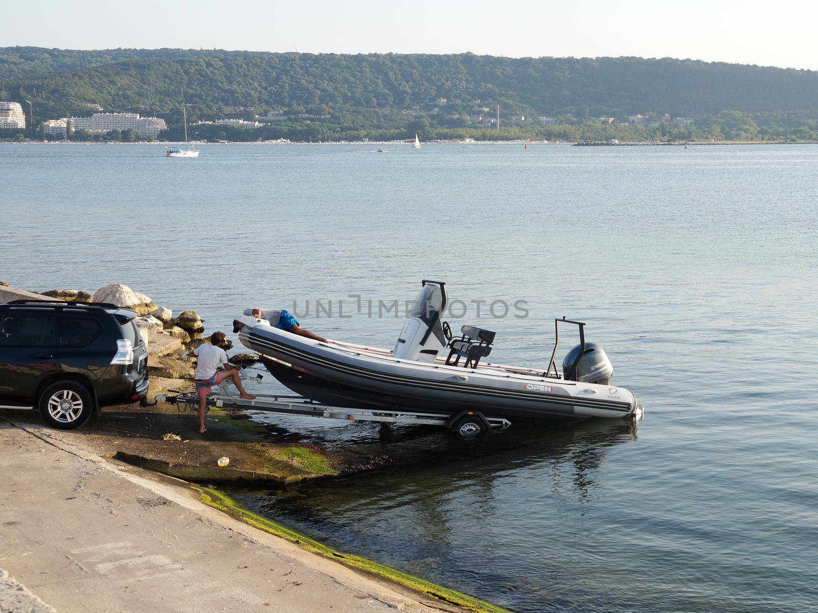 men pulling a boat onto a car trailer in the seaport by Annado