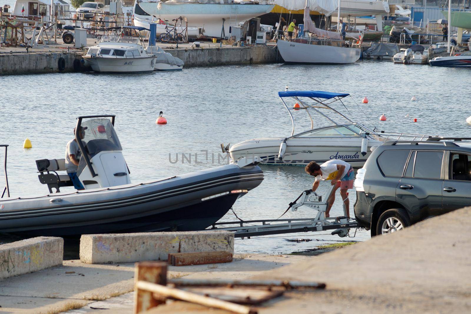 Varna, Bulgaria - July, 23, 2022: men loading a boat onto a car trailer in the seaport