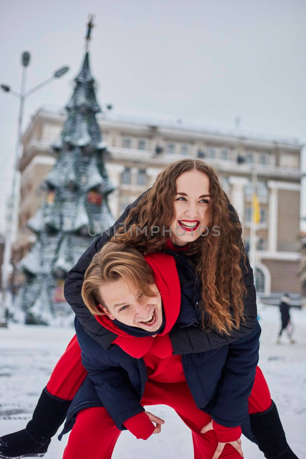 young family guy and girl spend the day in the park on a snowy day. Emotional young couple having fun while walking in the winter city, a lively man hugs his laughing beautiful woman. by mosfet_ua