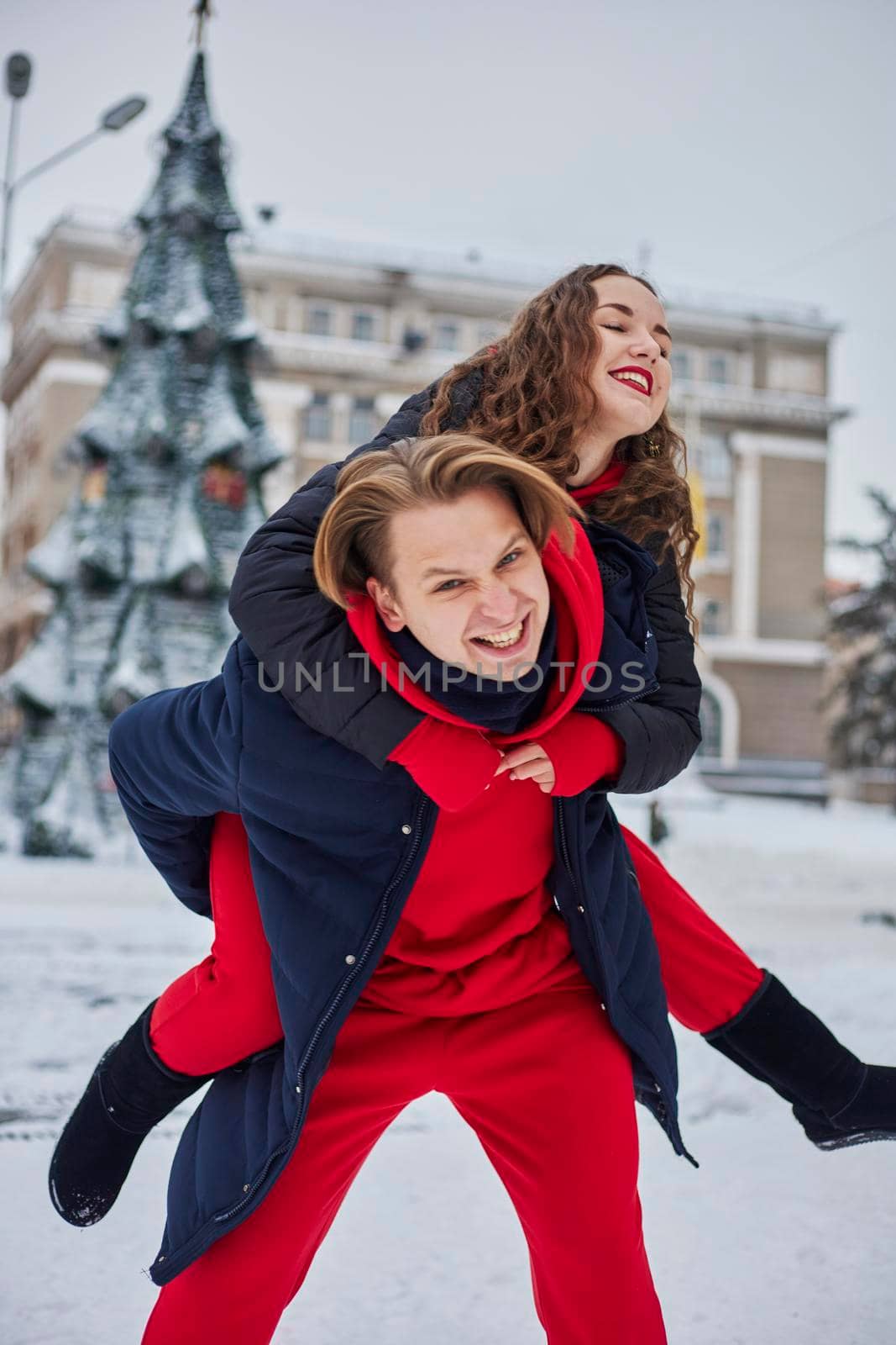 young family guy and girl spend the day in the park on a snowy day. Emotional young couple having fun while walking in the winter city, a lively man hugs his laughing beautiful woman