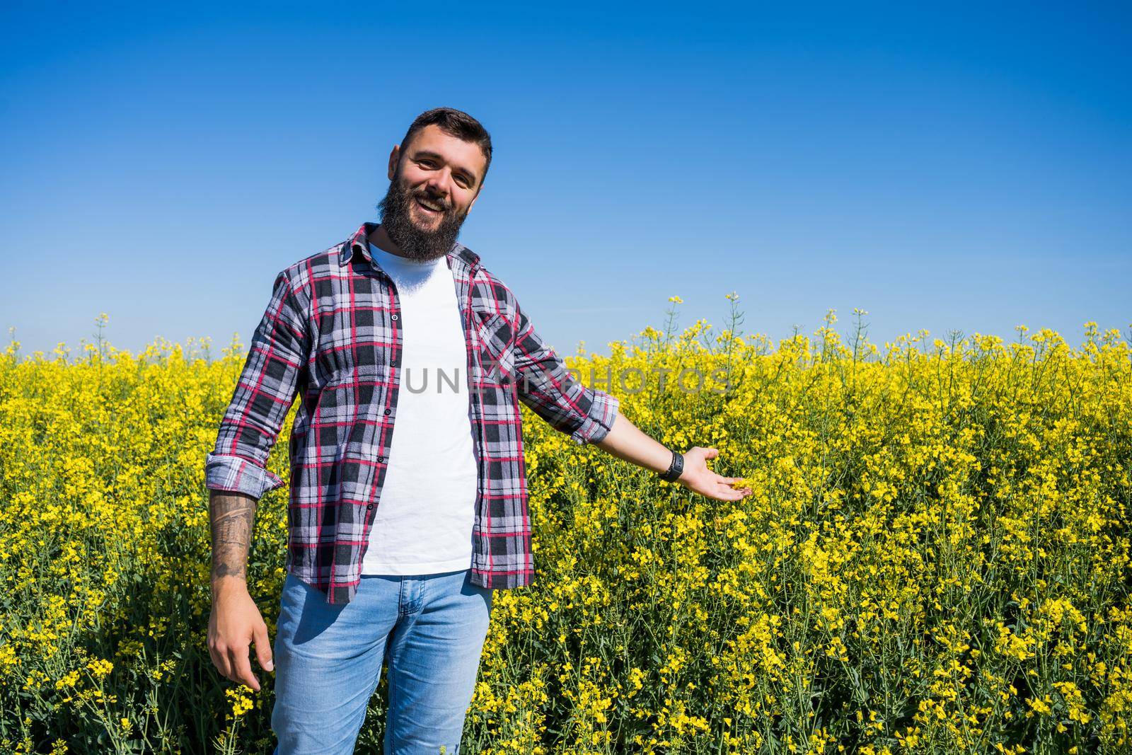 Portrait of happy and successful farmer who is standing by his rapeseed field. Rapeseed plantation in bloom.