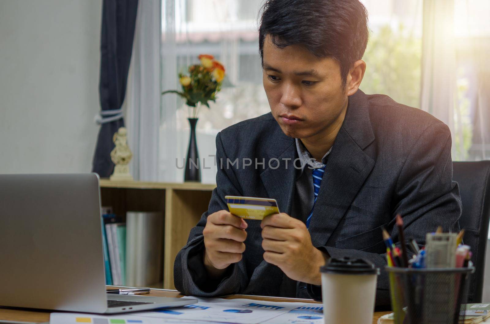 Businessman holding a credit card looking at documents graphs finances and economic investments at the computer with anxiety planning and online shopping with stress.