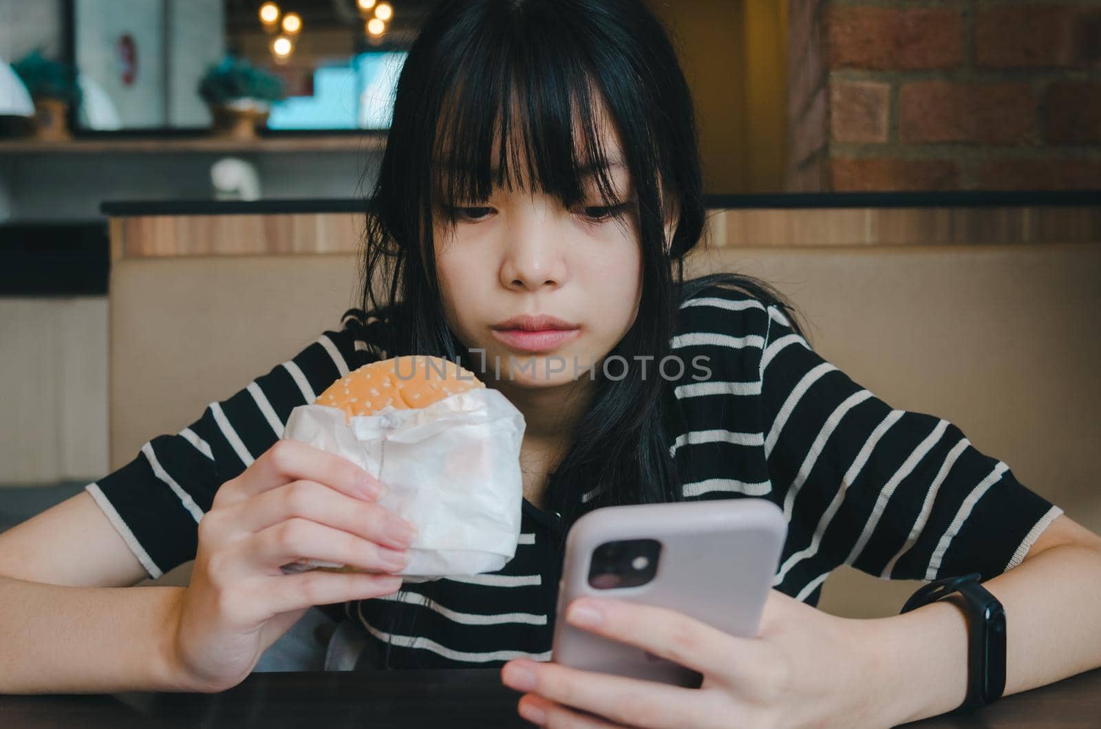 Female person holding mobile smartphone social network internet technology and eat hamburger fast food.
