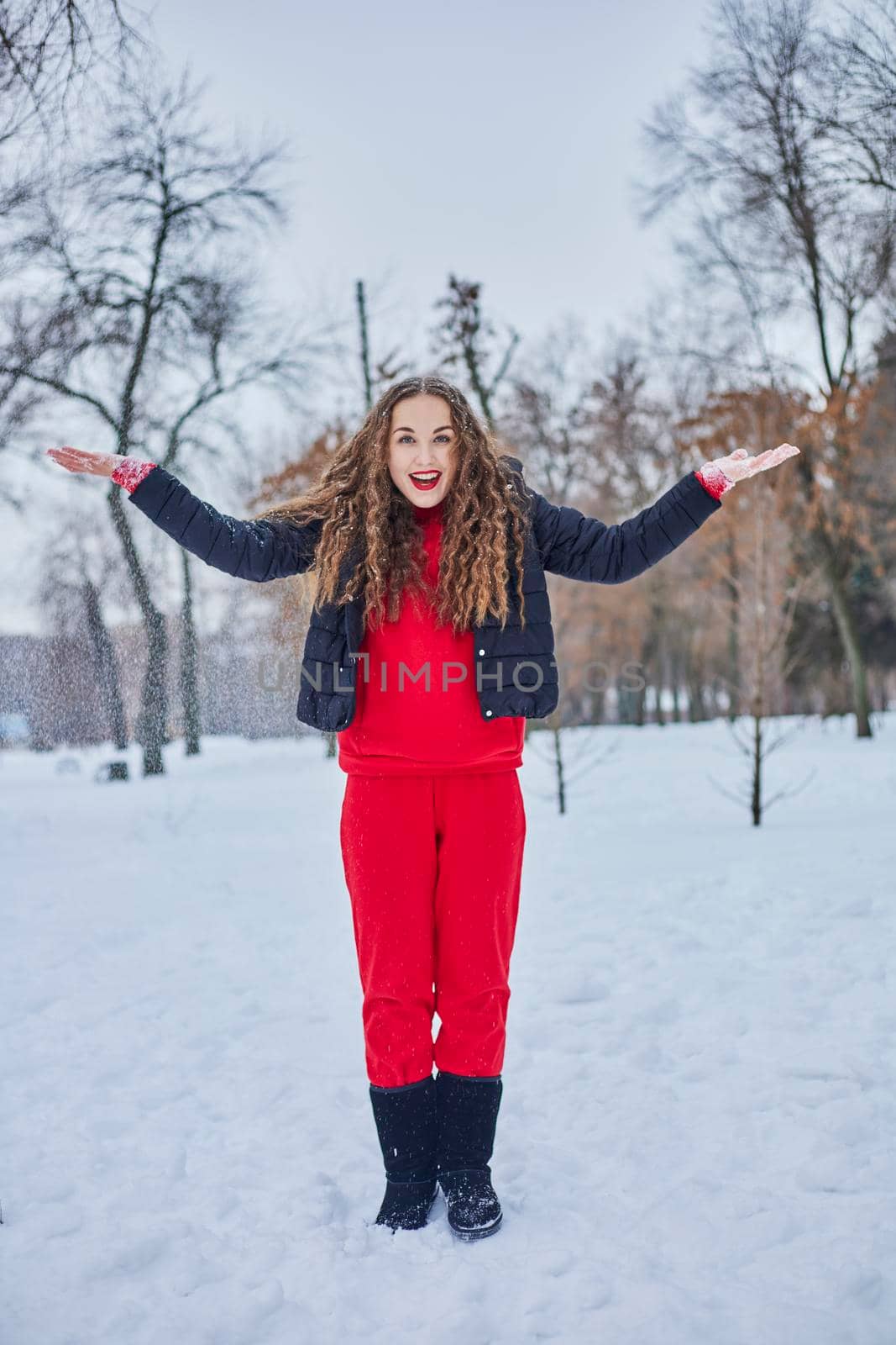 a young happy woman is having fun in a winter park, throwing snow, it is cold in her hands, the emissions are off scale. by mosfet_ua