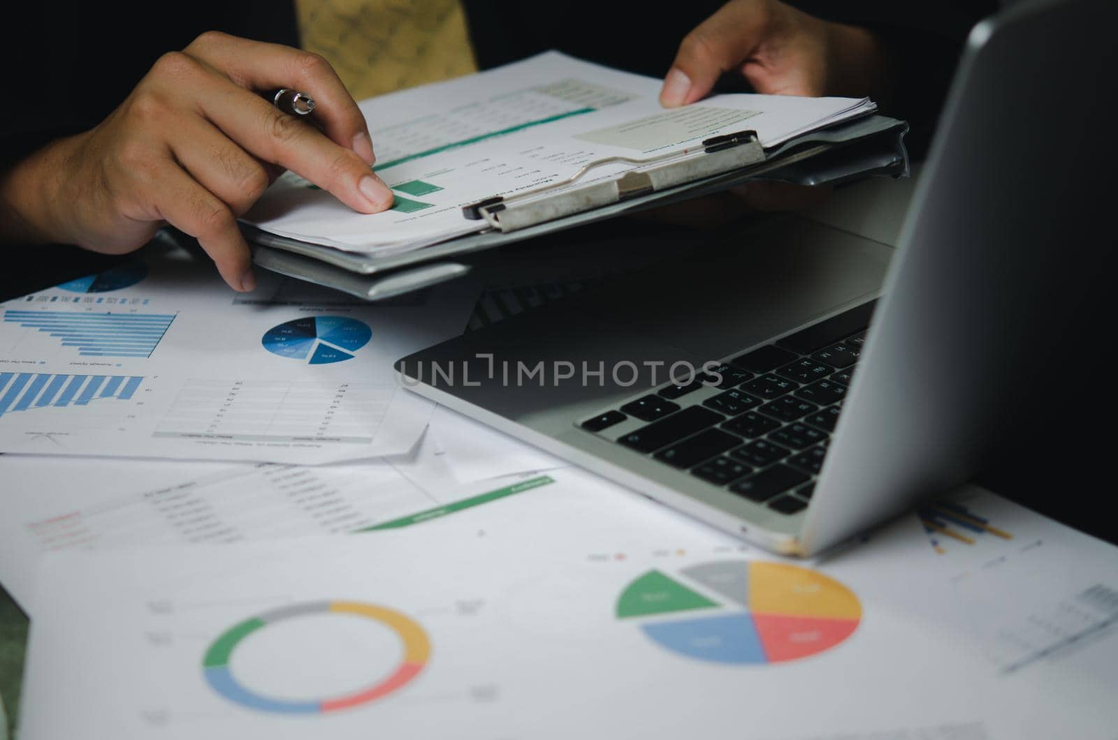 Businessman person pointing document graph financial marketing report and paperwork chart analysis investment with computer laptop on desk at office.