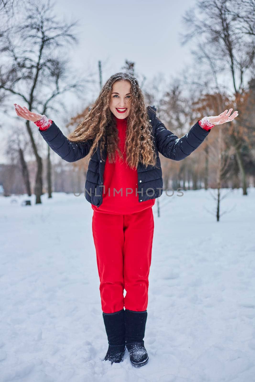 a young happy woman is having fun in a winter park, throwing snow, it is cold in her hands, the emissions are off scale