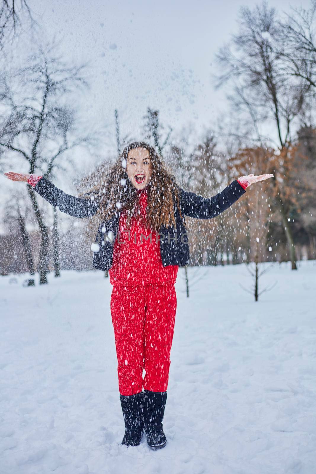 a young happy woman is having fun in a winter park, throwing snow, it is cold in her hands, the emissions are off scale. by mosfet_ua