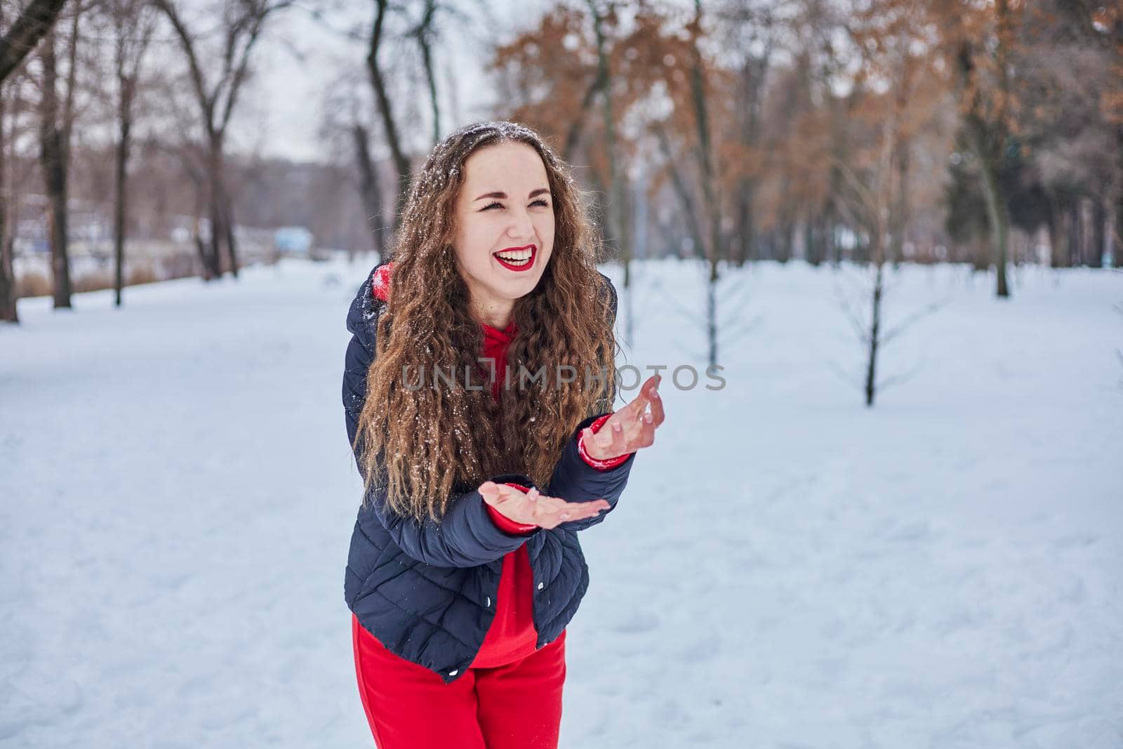 a young happy woman is having fun in a winter park, throwing snow, it is cold in her hands, the emissions are off scale