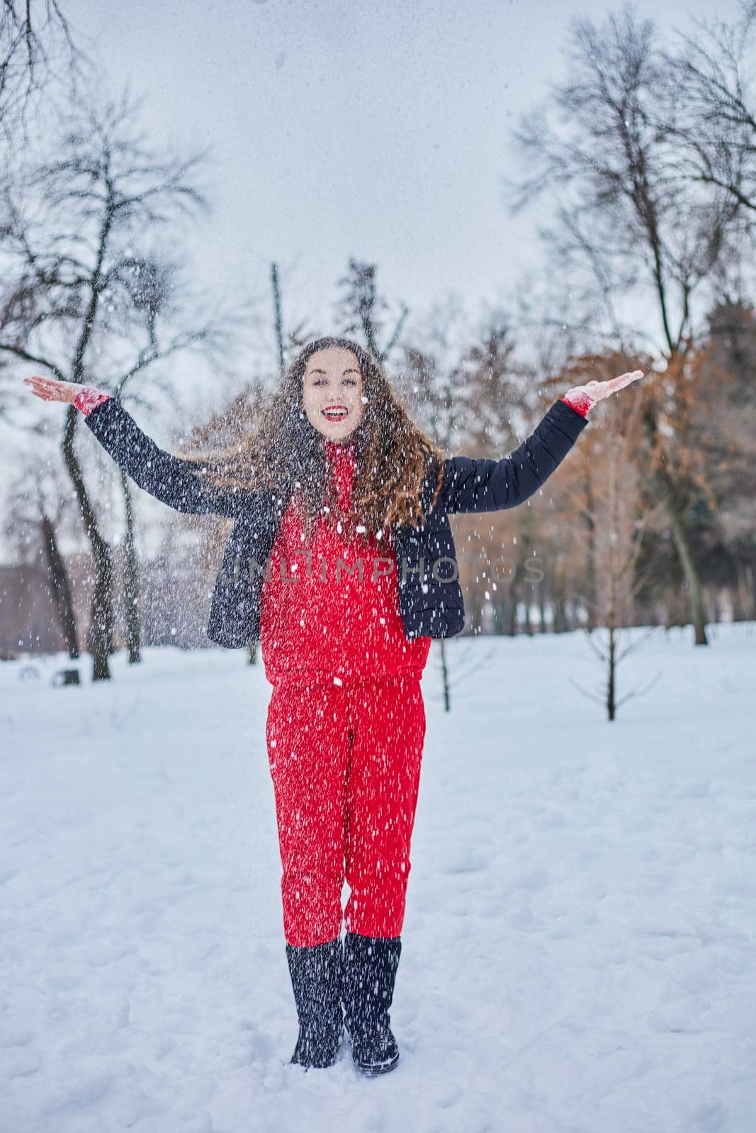 a young happy woman is having fun in a winter park, throwing snow, it is cold in her hands, the emissions are off scale. by mosfet_ua