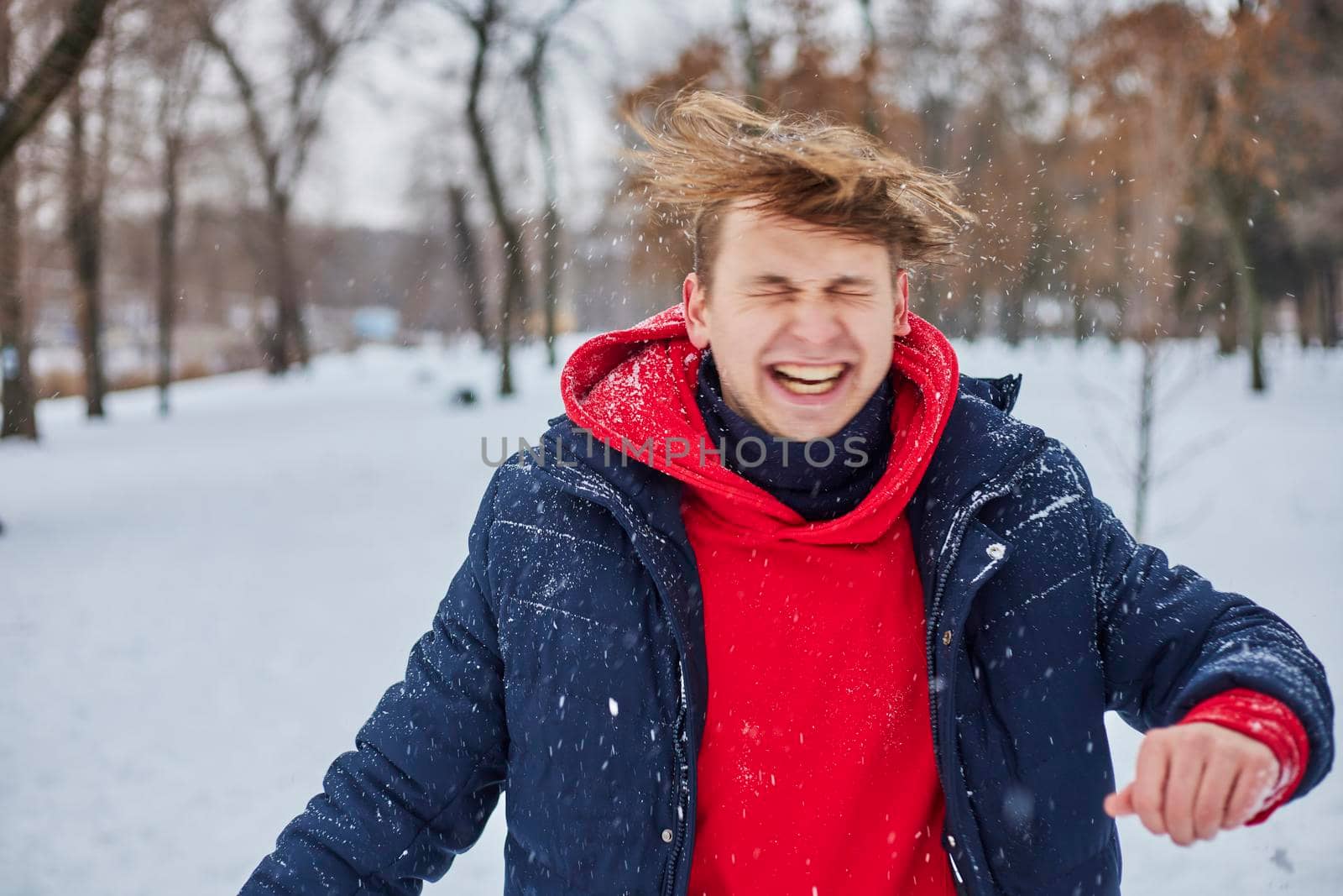 a young happy man is having fun in a winter park, throwing snow, it is cold in his hands, the emissions are off scale