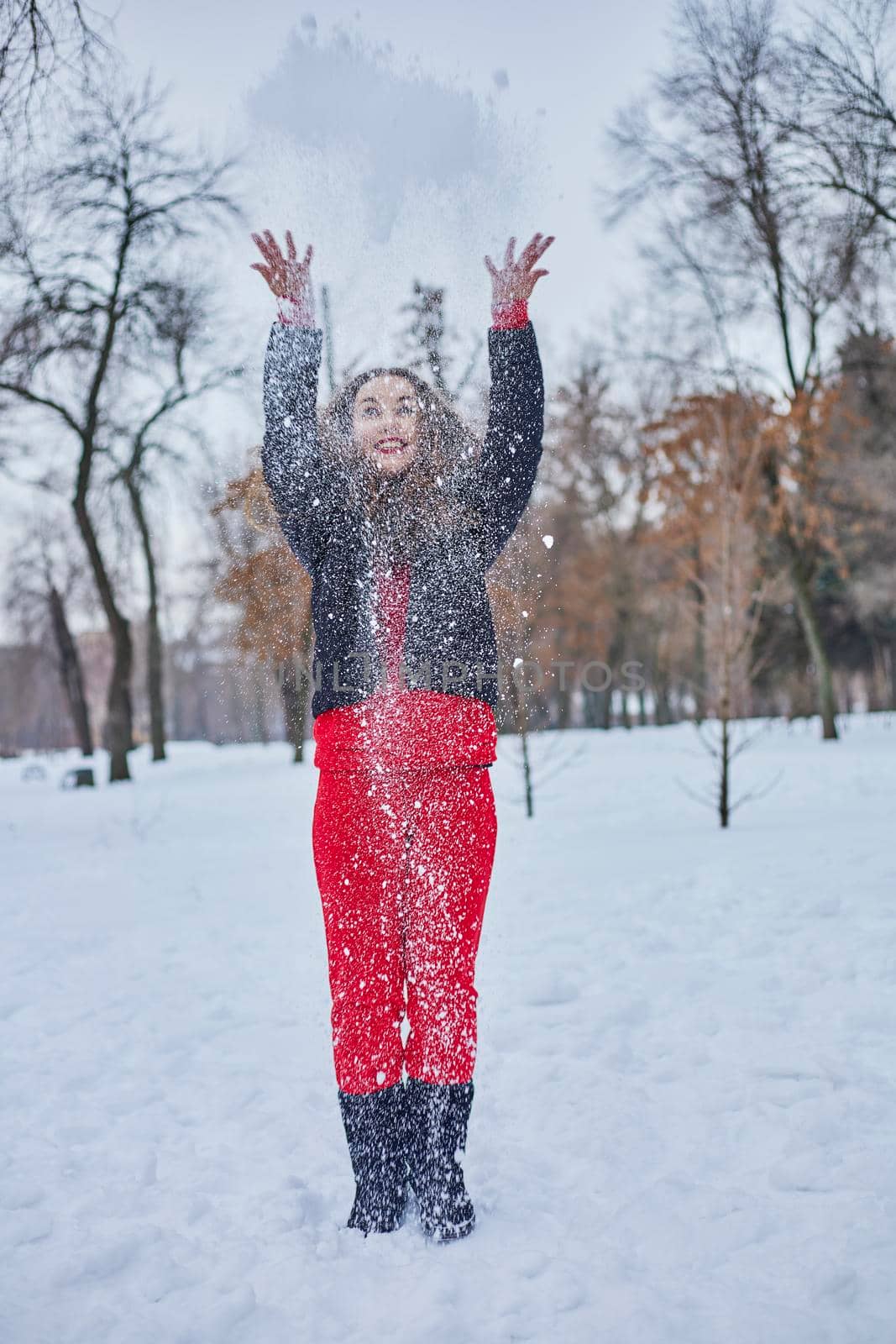 a young happy woman is having fun in a winter park, throwing snow, it is cold in her hands, the emissions are off scale