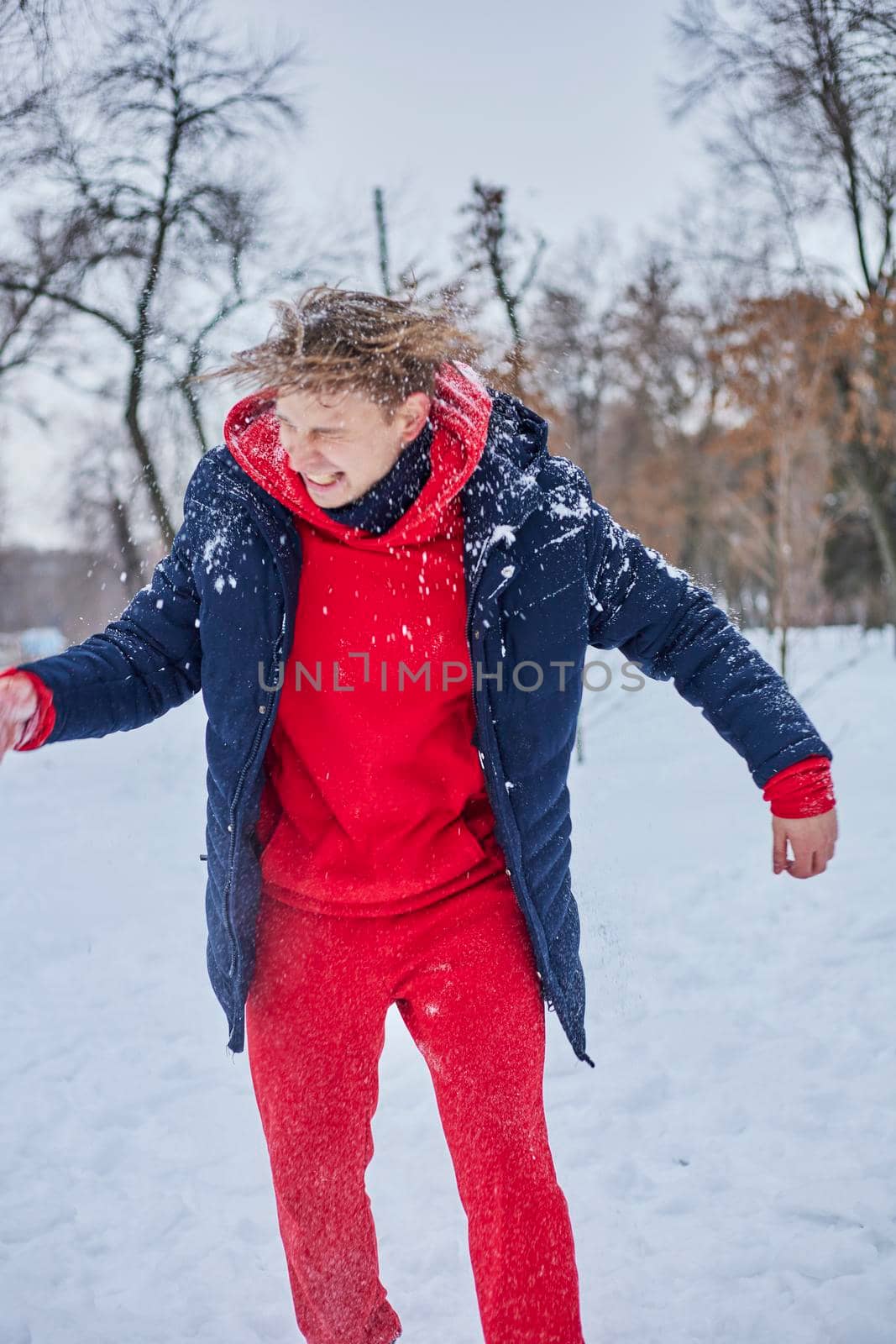 a young happy man is having fun in a winter park, throwing snow, it is cold in his hands, the emissions are off scale