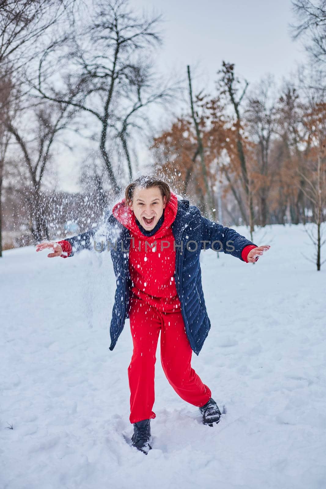 a young happy man is having fun in a winter park, throwing snow, it is cold in his hands, the emissions are off scale. by mosfet_ua