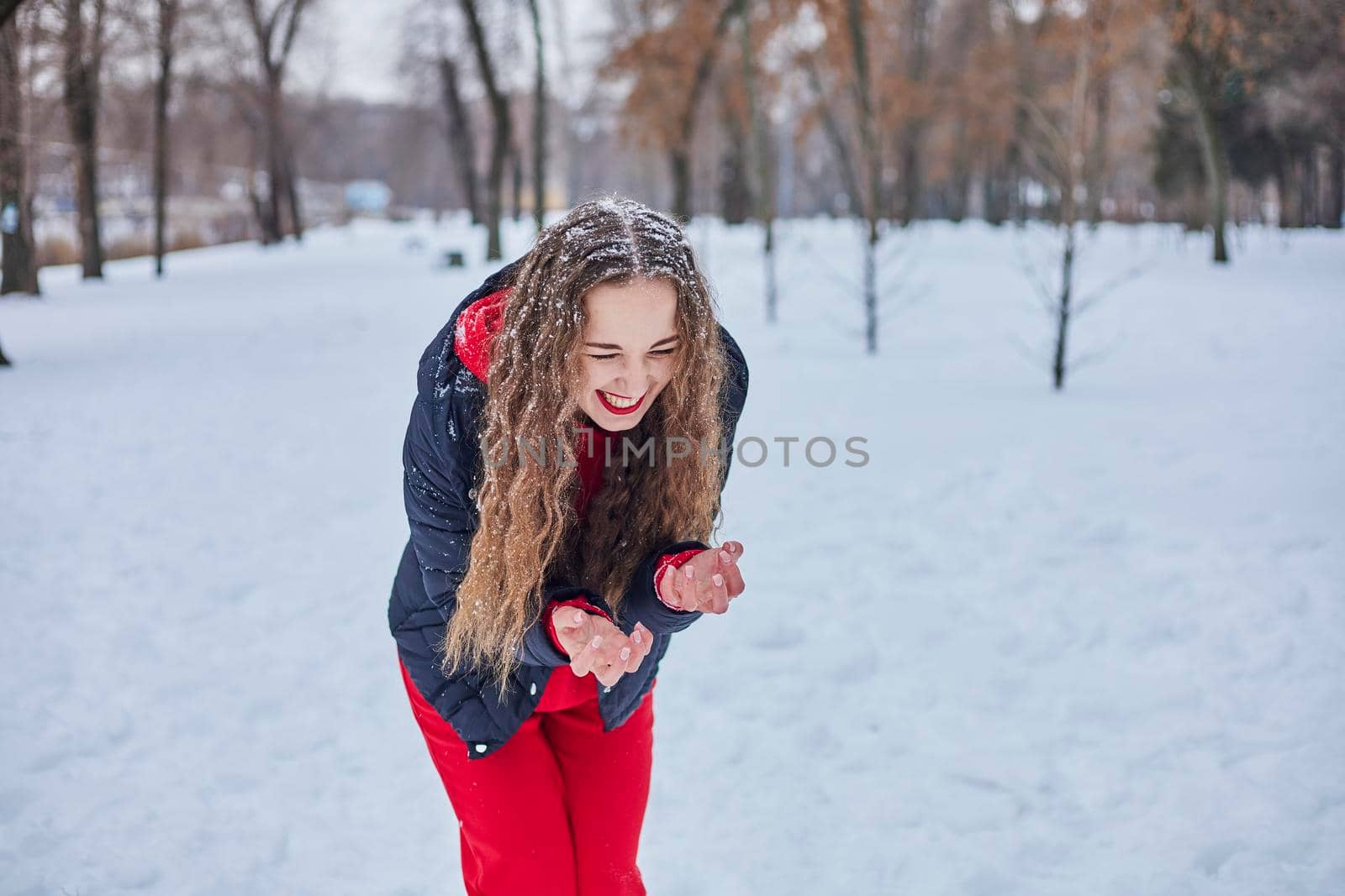 a young happy woman is having fun in a winter park, throwing snow, it is cold in her hands, the emissions are off scale