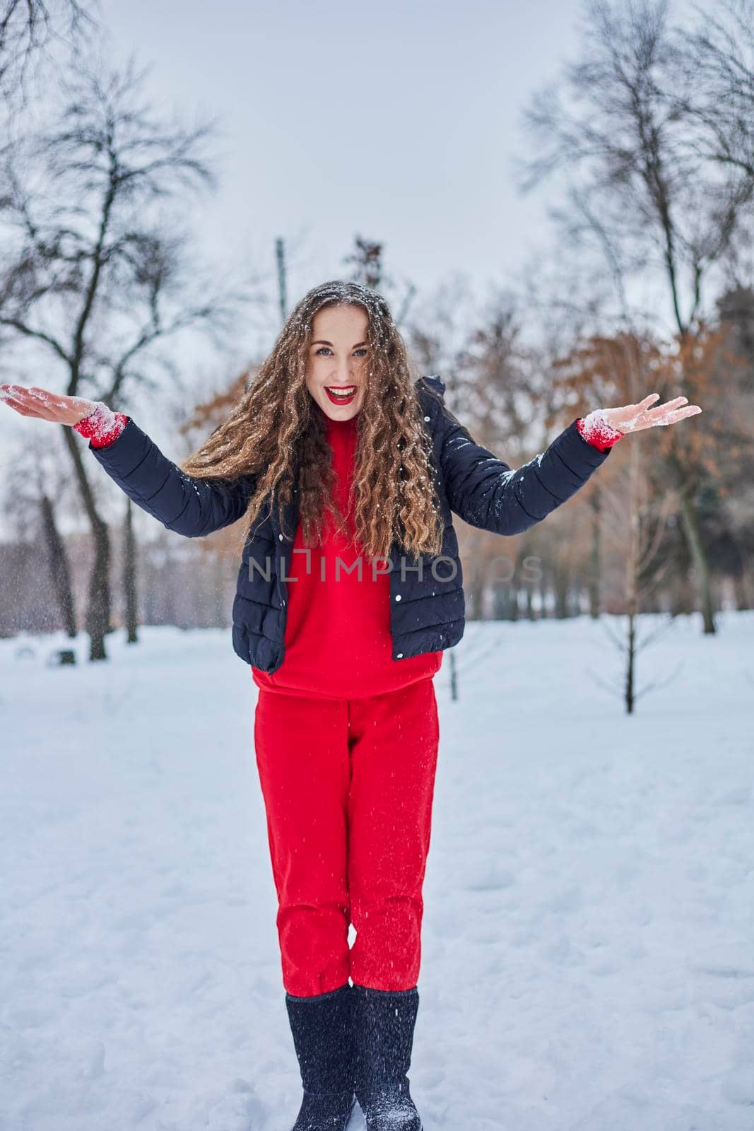 a young happy woman is having fun in a winter park, throwing snow, it is cold in her hands, the emissions are off scale. by mosfet_ua