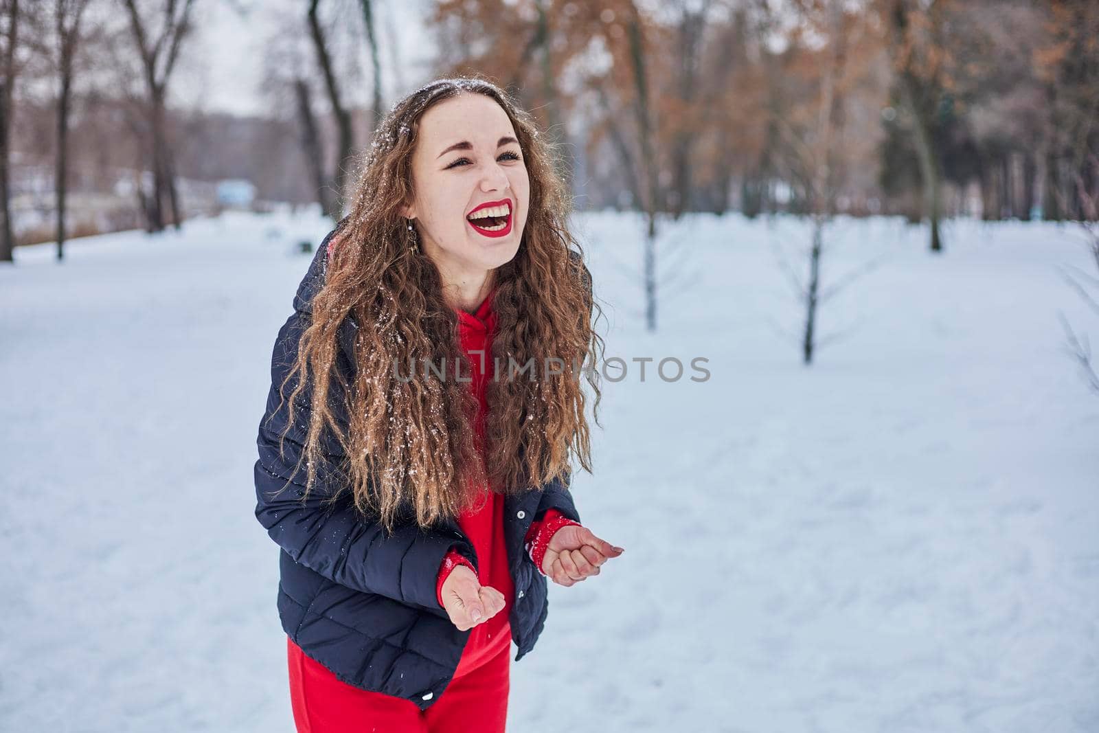 a young happy woman is having fun in a winter park, throwing snow, it is cold in her hands, the emissions are off scale