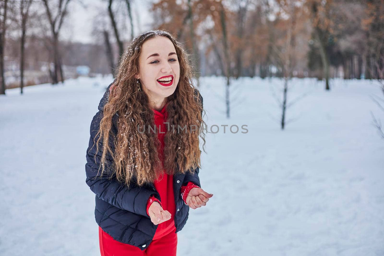 a young happy woman is having fun in a winter park, throwing snow, it is cold in her hands, the emissions are off scale. by mosfet_ua