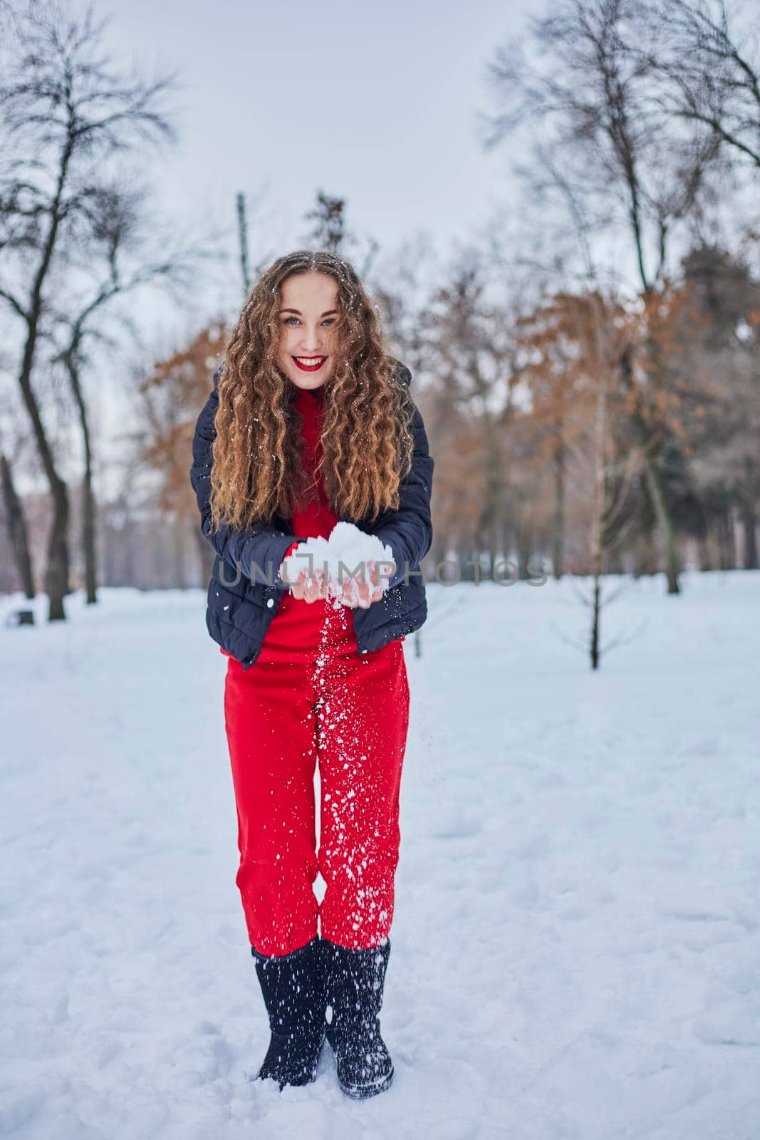 a young happy woman is having fun in a winter park, throwing snow, it is cold in her hands, the emissions are off scale. by mosfet_ua