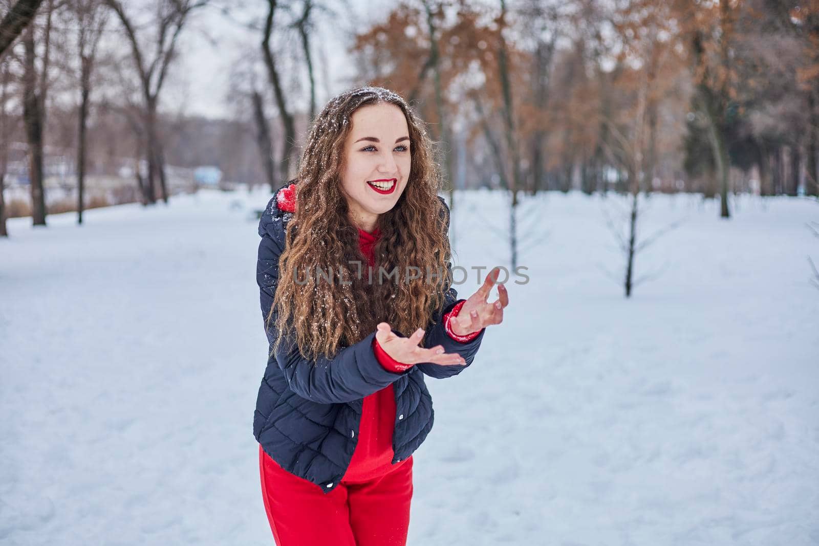 a young happy woman is having fun in a winter park, throwing snow, it is cold in her hands, the emissions are off scale. by mosfet_ua