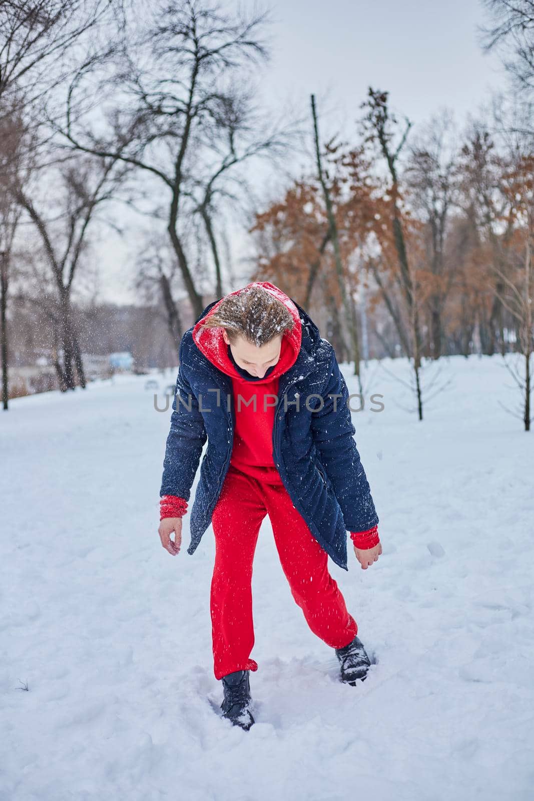 a young happy man is having fun in a winter park, throwing snow, it is cold in his hands, the emissions are off scale