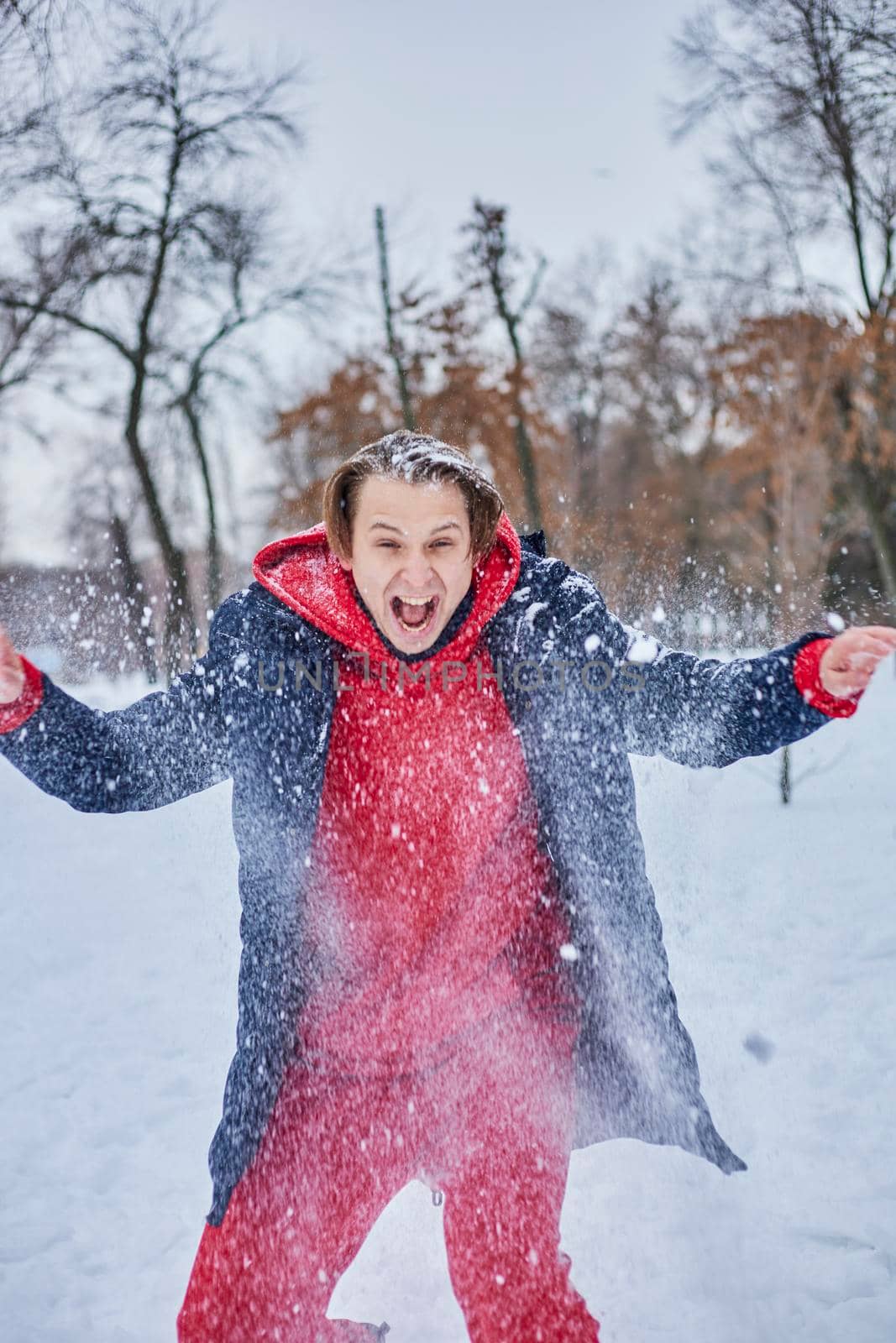 a young happy man is having fun in a winter park, throwing snow, it is cold in his hands, the emissions are off scale. by mosfet_ua