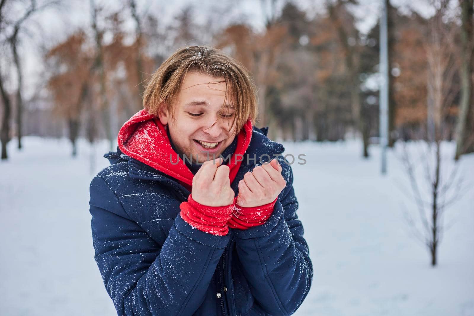 a young happy man is having fun in a winter park, throwing snow, it is cold in his hands, the emissions are off scale. by mosfet_ua