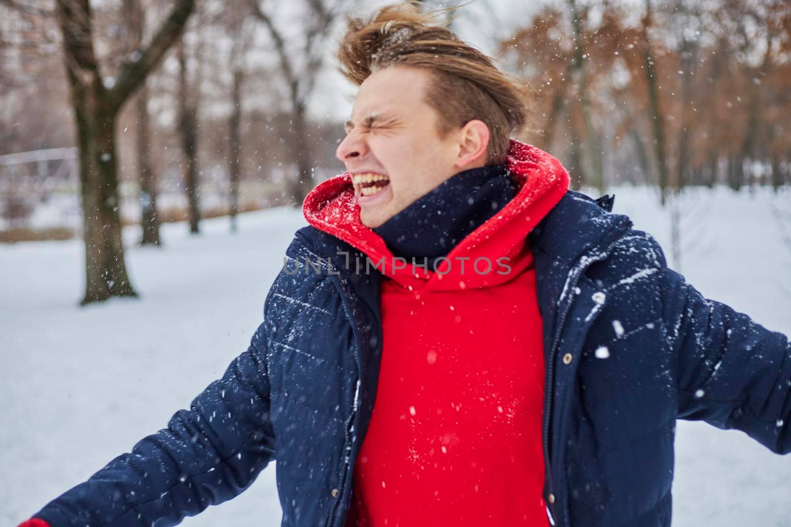 a young happy man is having fun in a winter park, throwing snow, it is cold in his hands, the emissions are off scale. by mosfet_ua