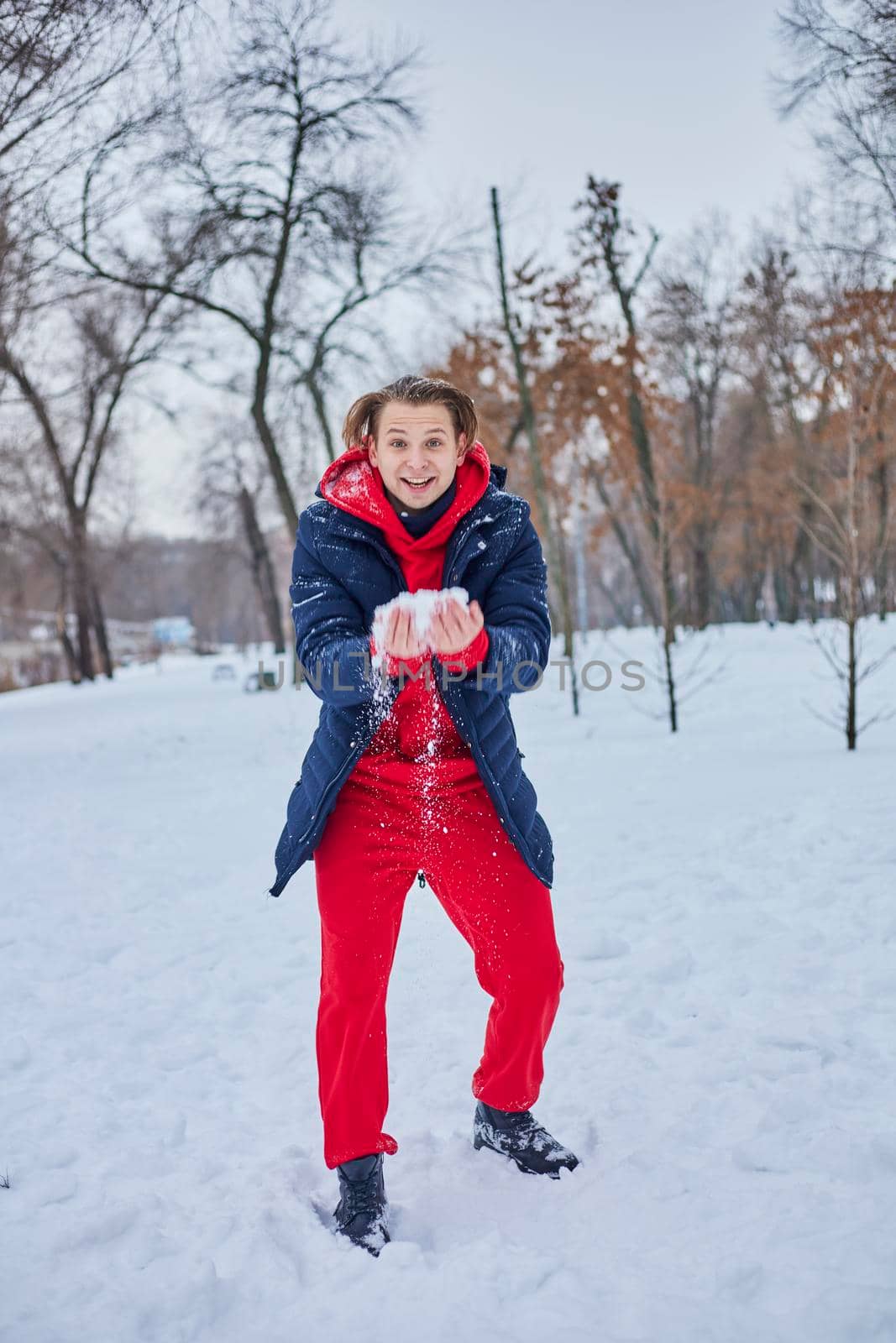 a young happy man is having fun in a winter park, throwing snow, it is cold in his hands, the emissions are off scale