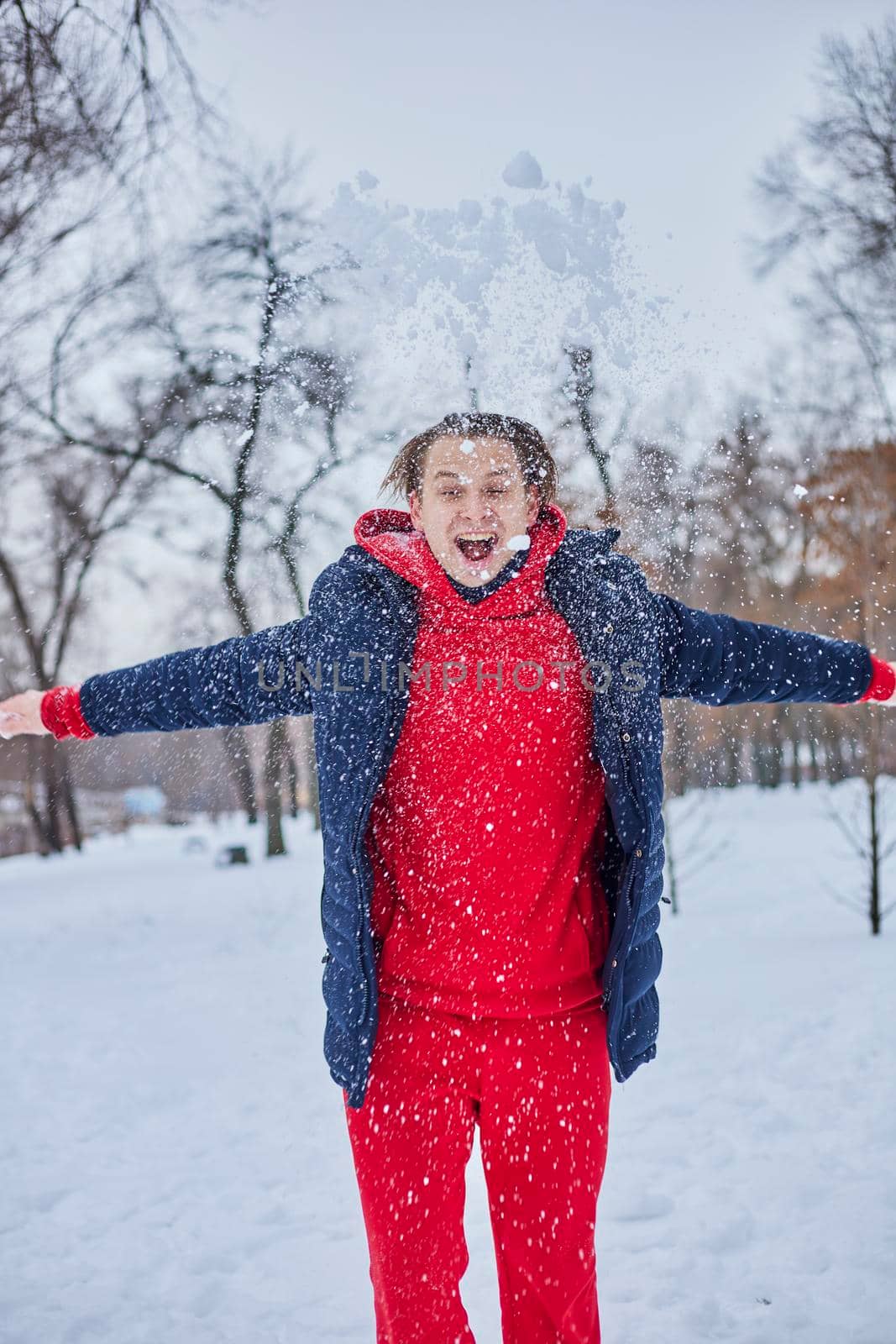 a young happy man is having fun in a winter park, throwing snow, it is cold in his hands, the emissions are off scale. by mosfet_ua