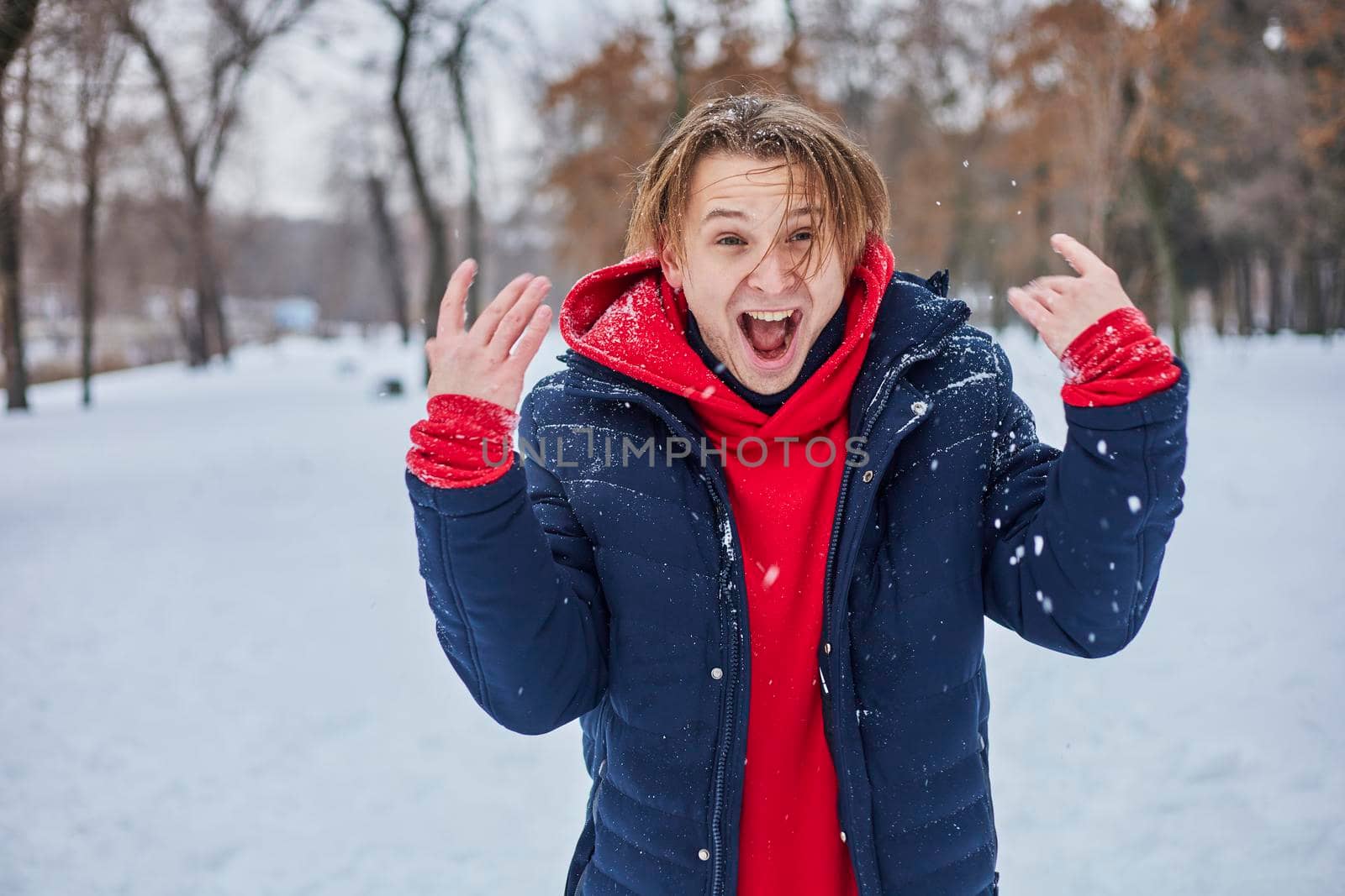 a young happy man is having fun in a winter park, throwing snow, it is cold in his hands, the emissions are off scale