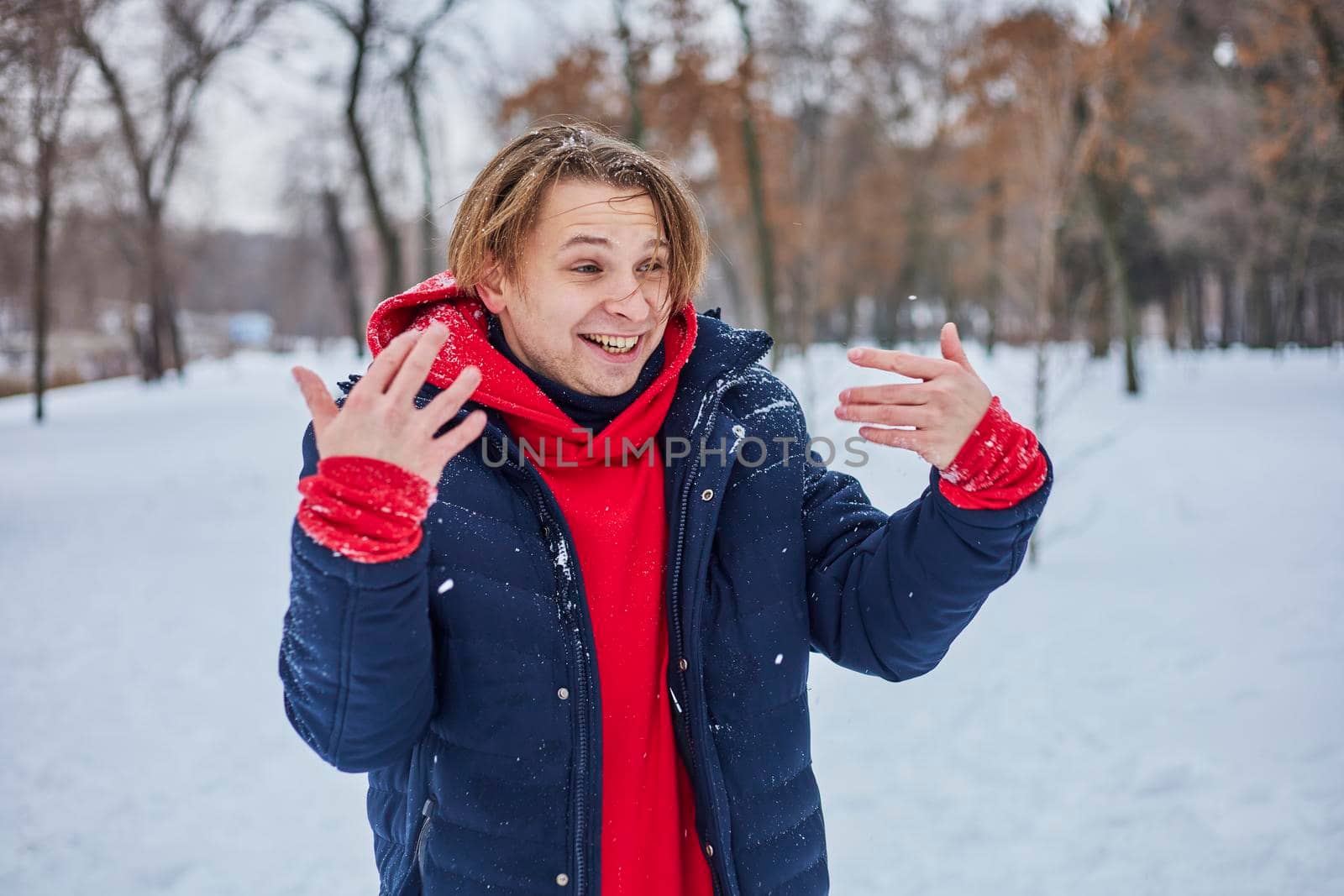 a young happy man is having fun in a winter park, throwing snow, it is cold in his hands, the emissions are off scale