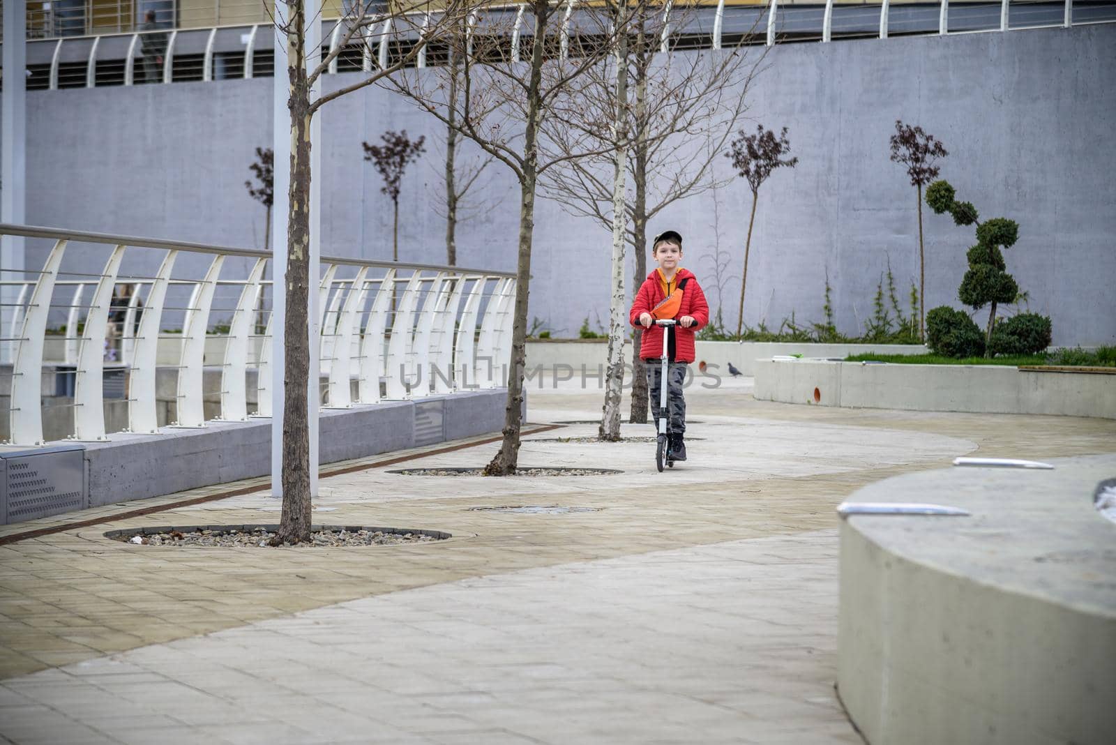 Happy family lifestyle and holiday concept. One little boy riding scooter, walking in city, street. Having fun alone.