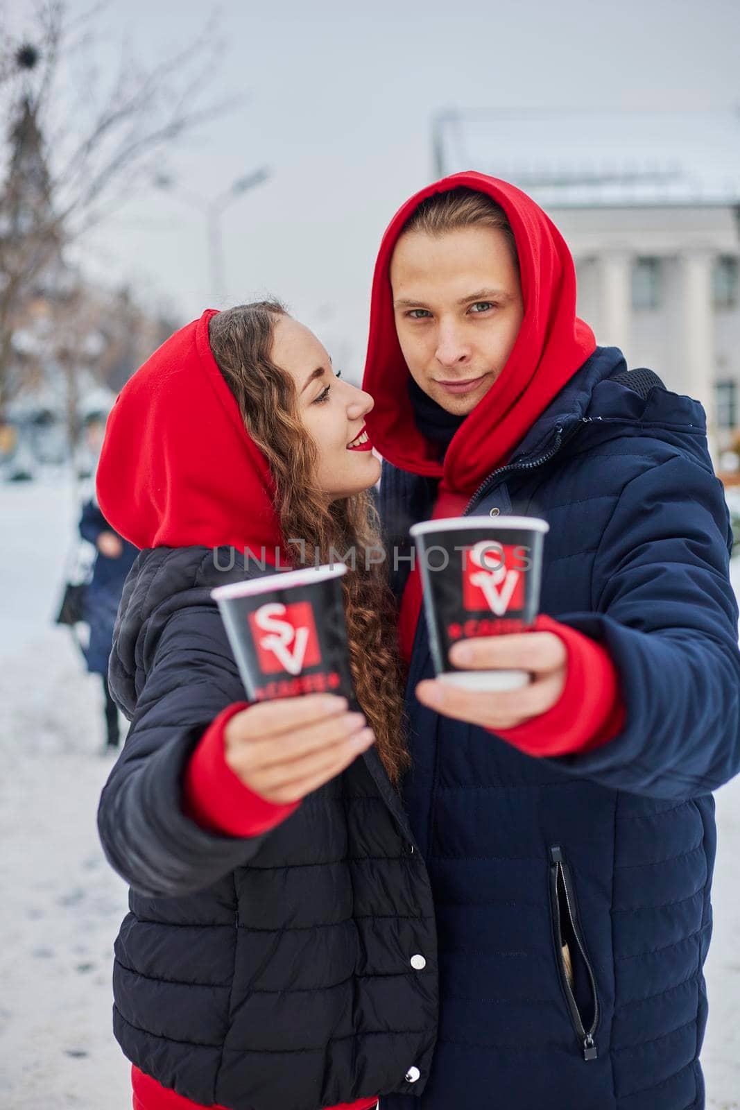 young family guy and girl spend the day in the park on a snowy day. the guy hugs the girl while standing on the street, they drink coffee together