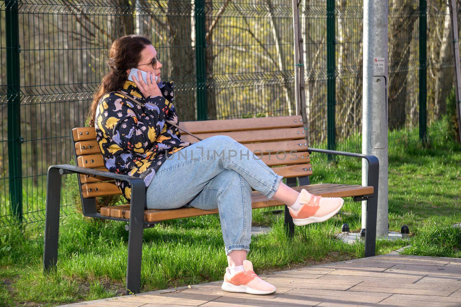 Young beautiful woman sitting on a bench in the city park and speaking on the phone.